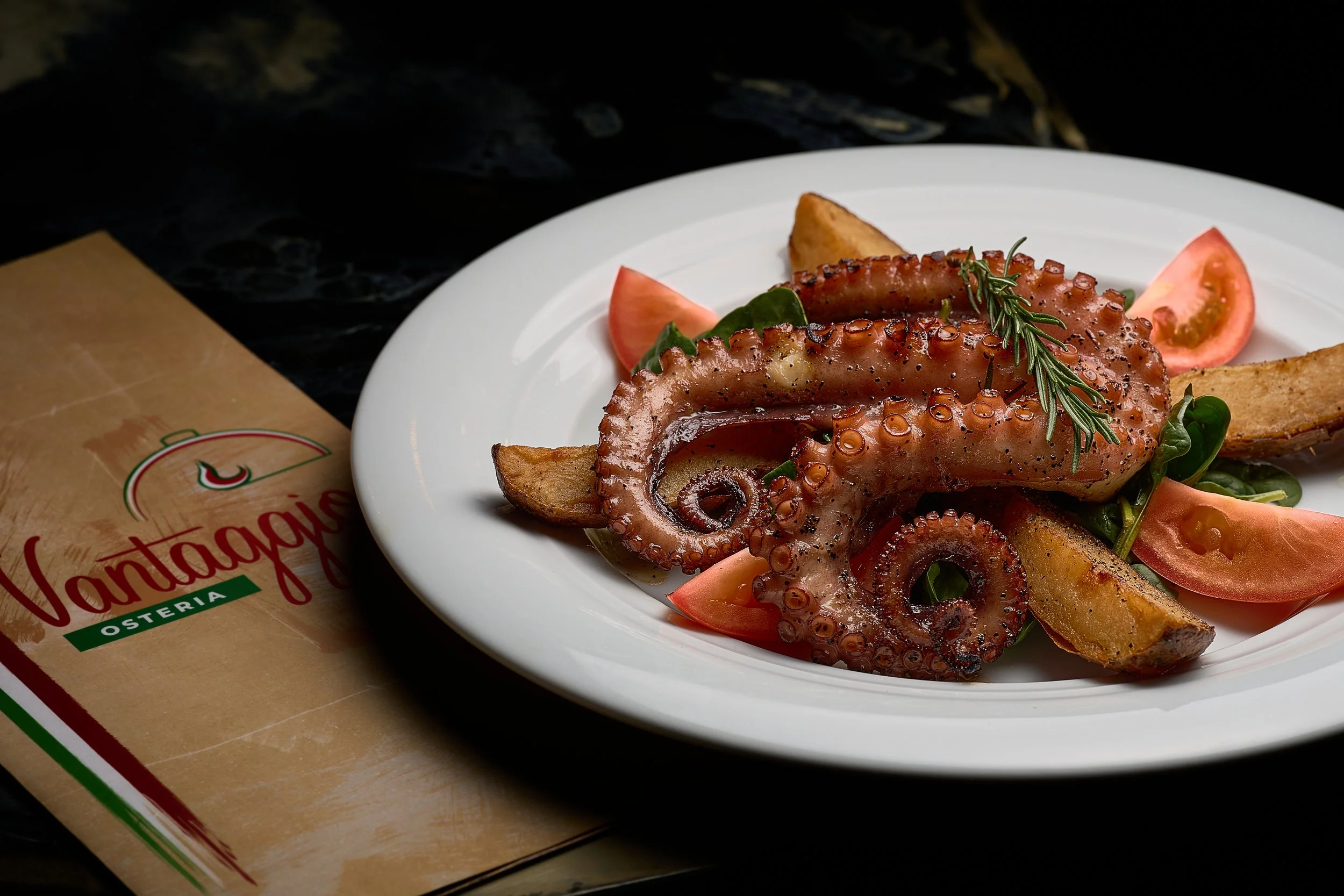 Pulpo a la parrilla con papas fritas, tomates y romero en un plato blanco.