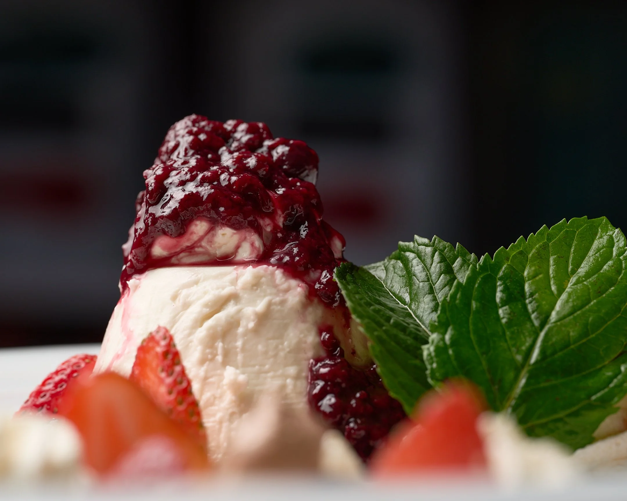 Postre de queso con salsa de frutos rojos, fresa y hoja de menta