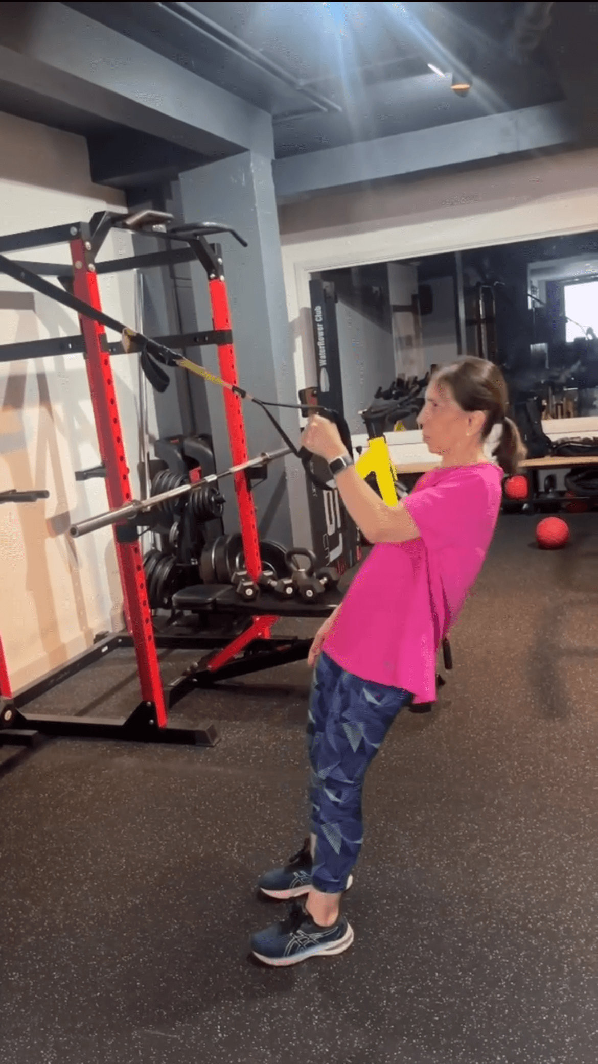 A female client over 60 using TRX suspension training for strength and mobility in a private gym