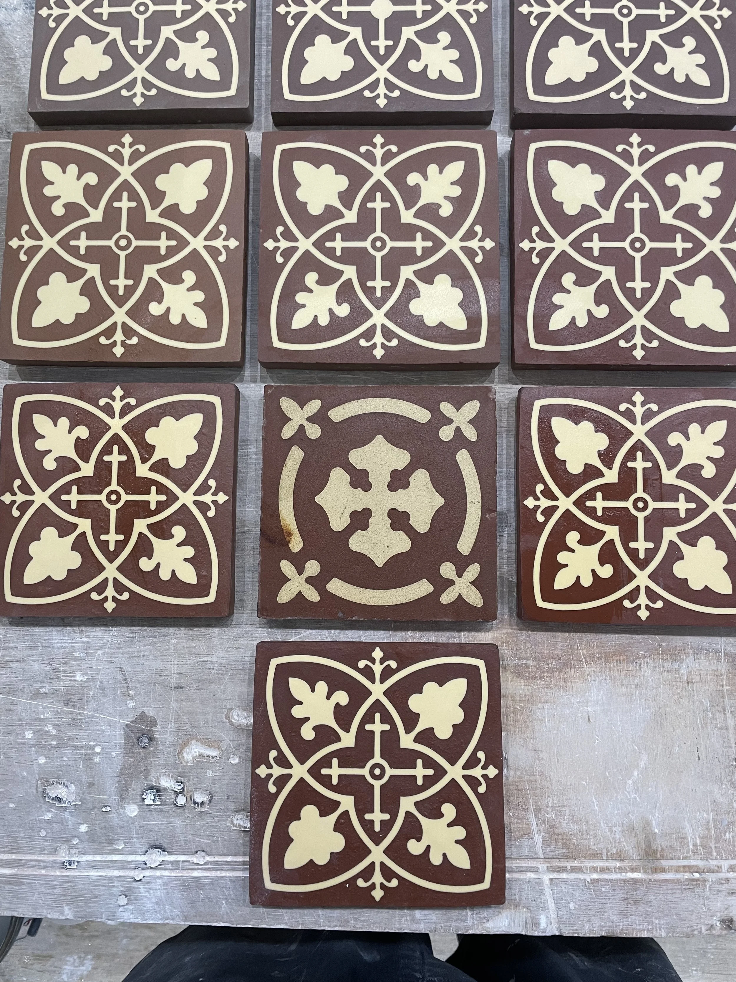 A group of decorative tiles with a floral and geometric pattern in cream and brown colors, arranged on a surface.