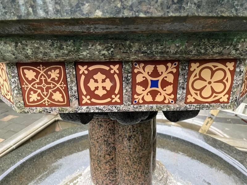 Close-up of decorative tiles with floral and geometric patterns on the edge of a stone fountain.