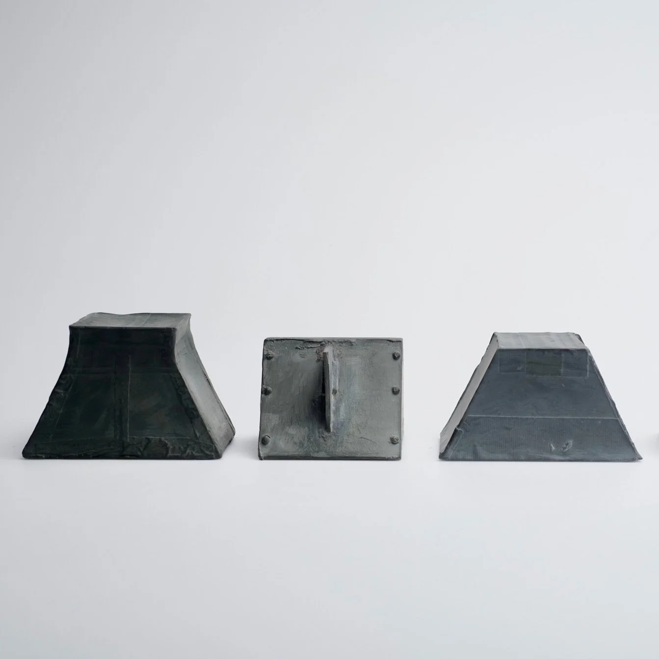 Four gray metallic pyramid-shaped ceramic objects placed in a row against a white background.