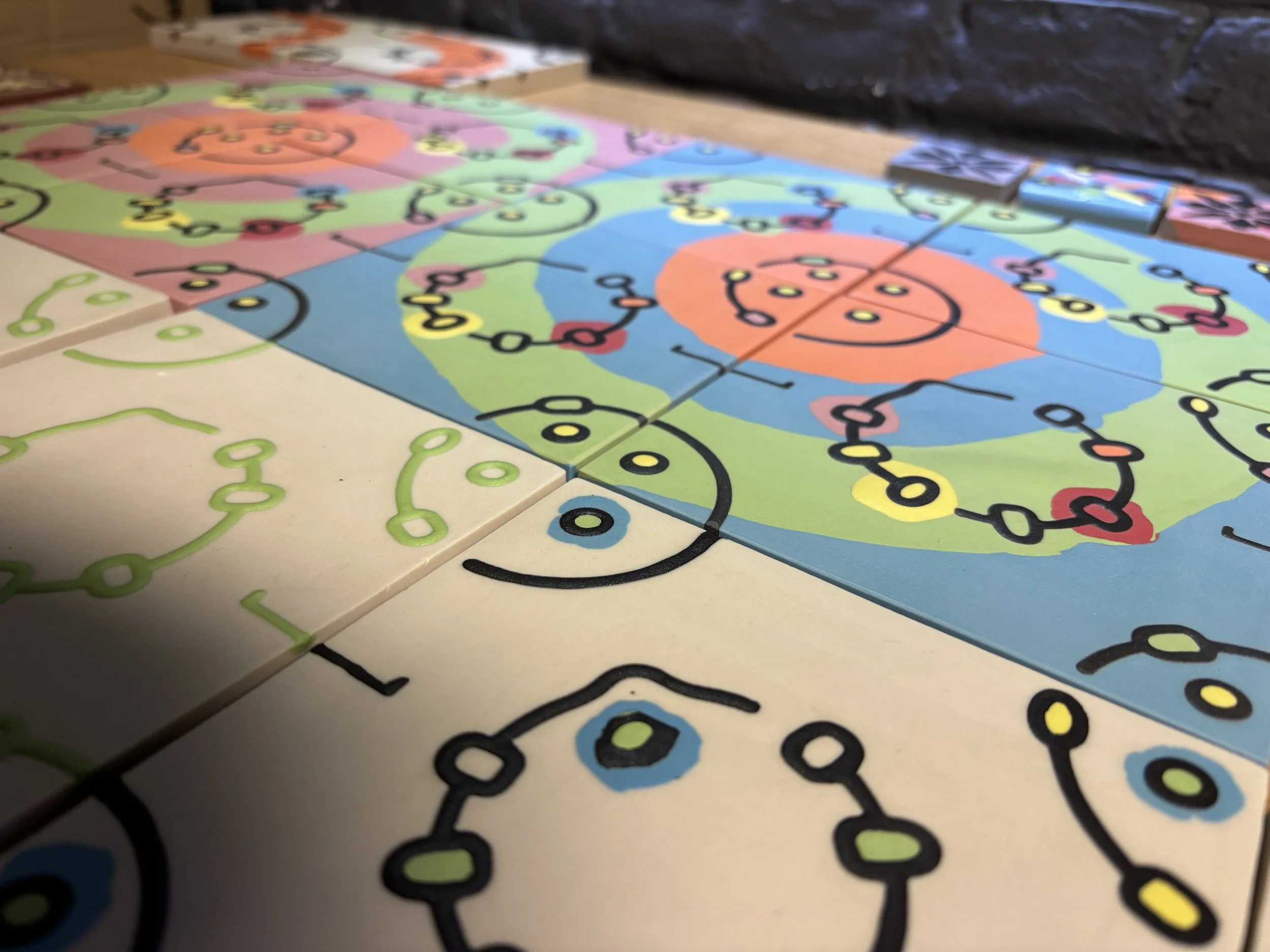 Close-up of a colourful selection of various Conidiobolus encaustic tiles with interconnected lines on tiles featuring bright colors like pink, blue, green, orange, and black lines.