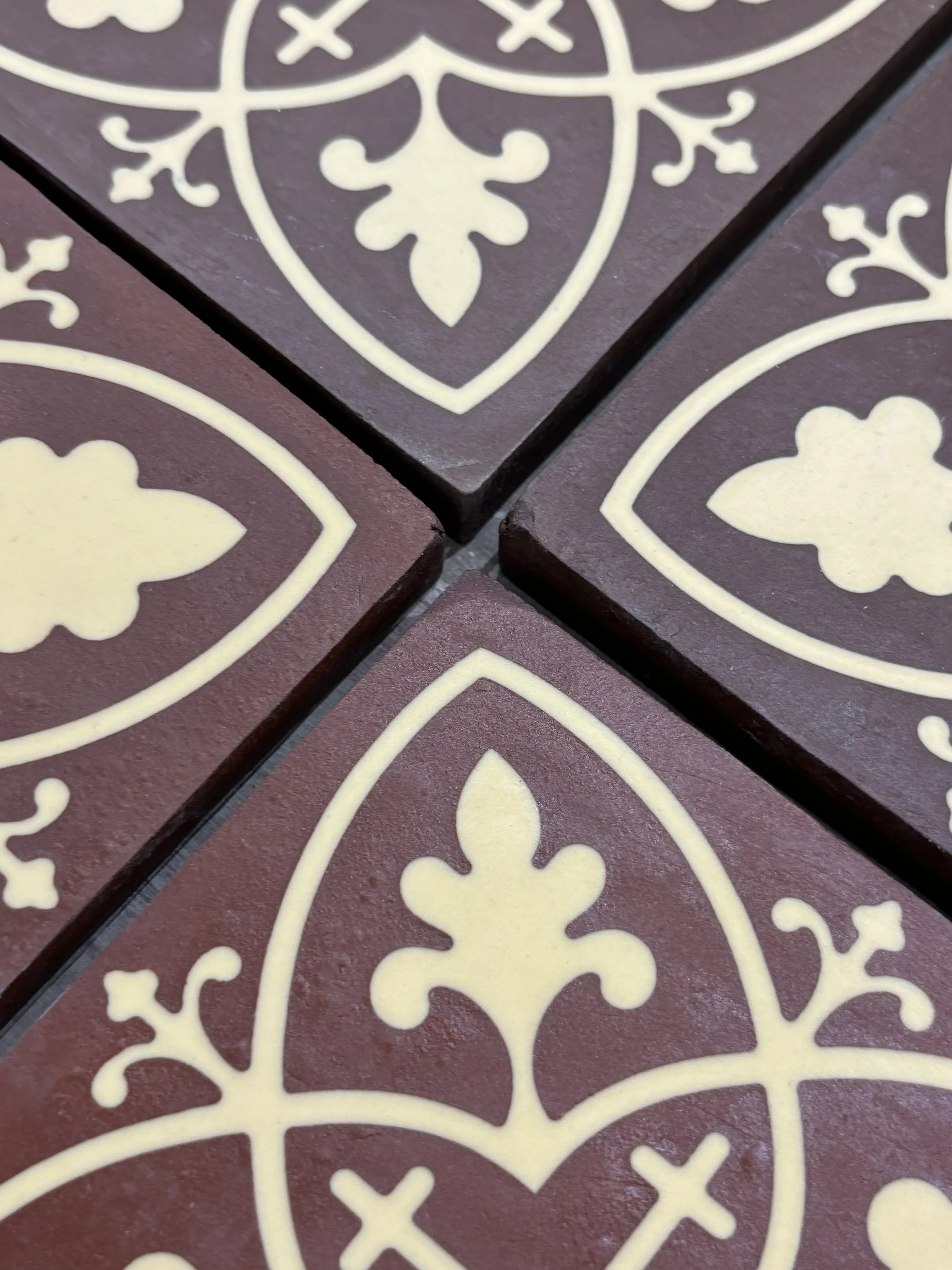 Close-up of patterned ceramic tiles with a burgundy background and cream-colored intricate floral and leaf motifs.