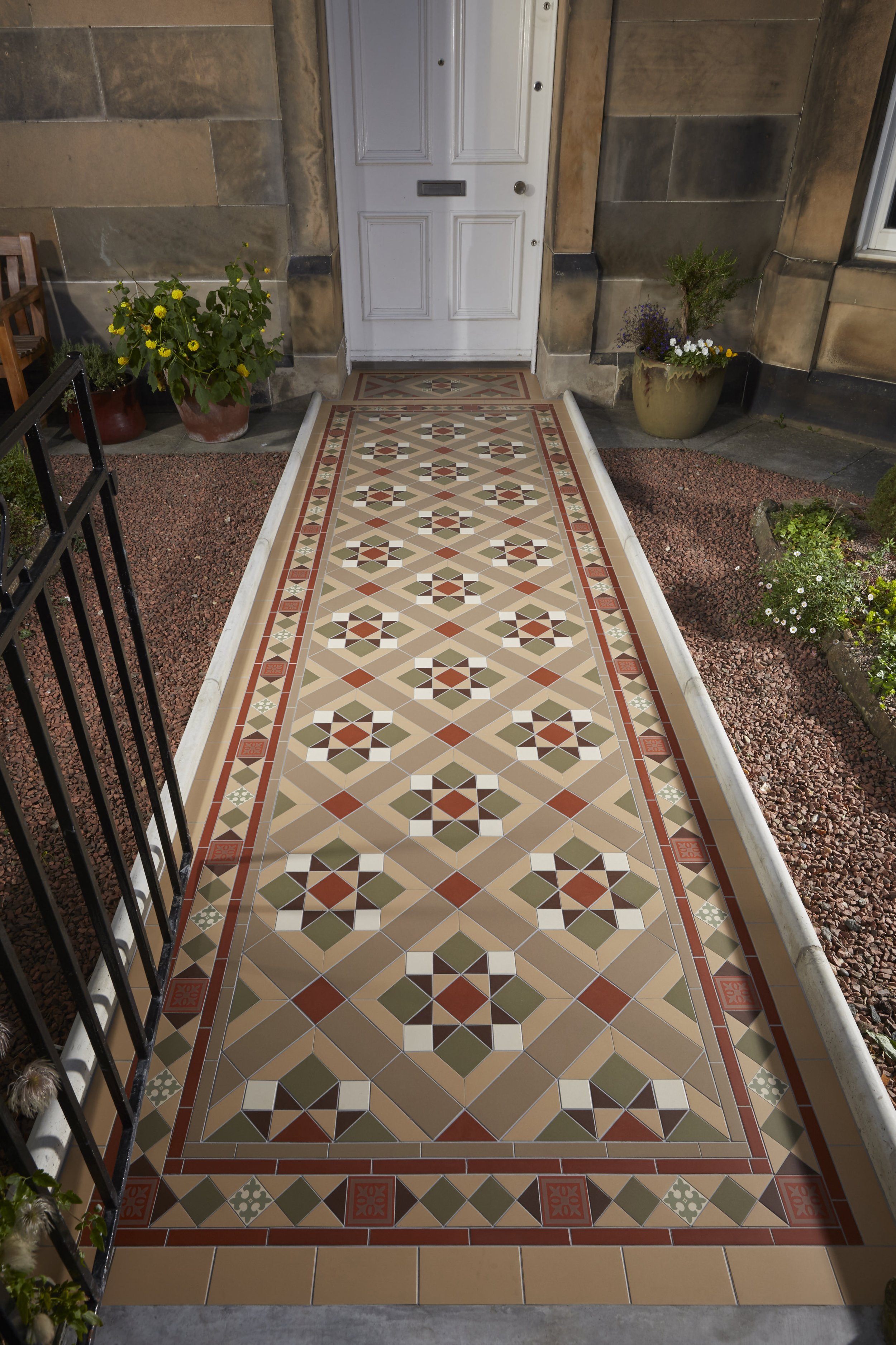 Decorative tiled pathway leading to a white front door, flanked by potted plants and surrounded by gravel garden beds.