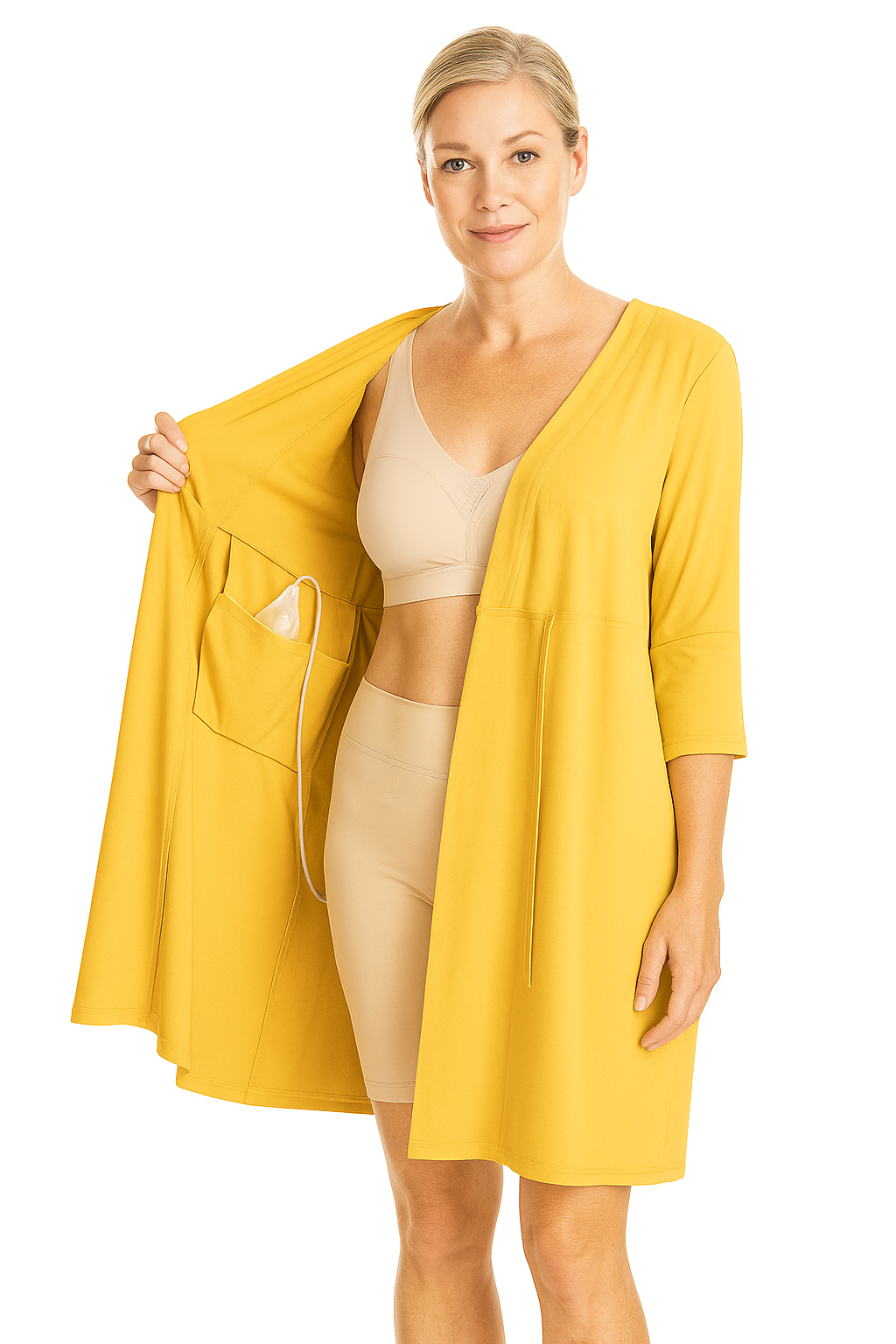 Une femme en vêtements beige et un long manteau jaune tient la doublure de son manteau ouverte, révélant un dispositif médical avec un fil connecté dans la poche.