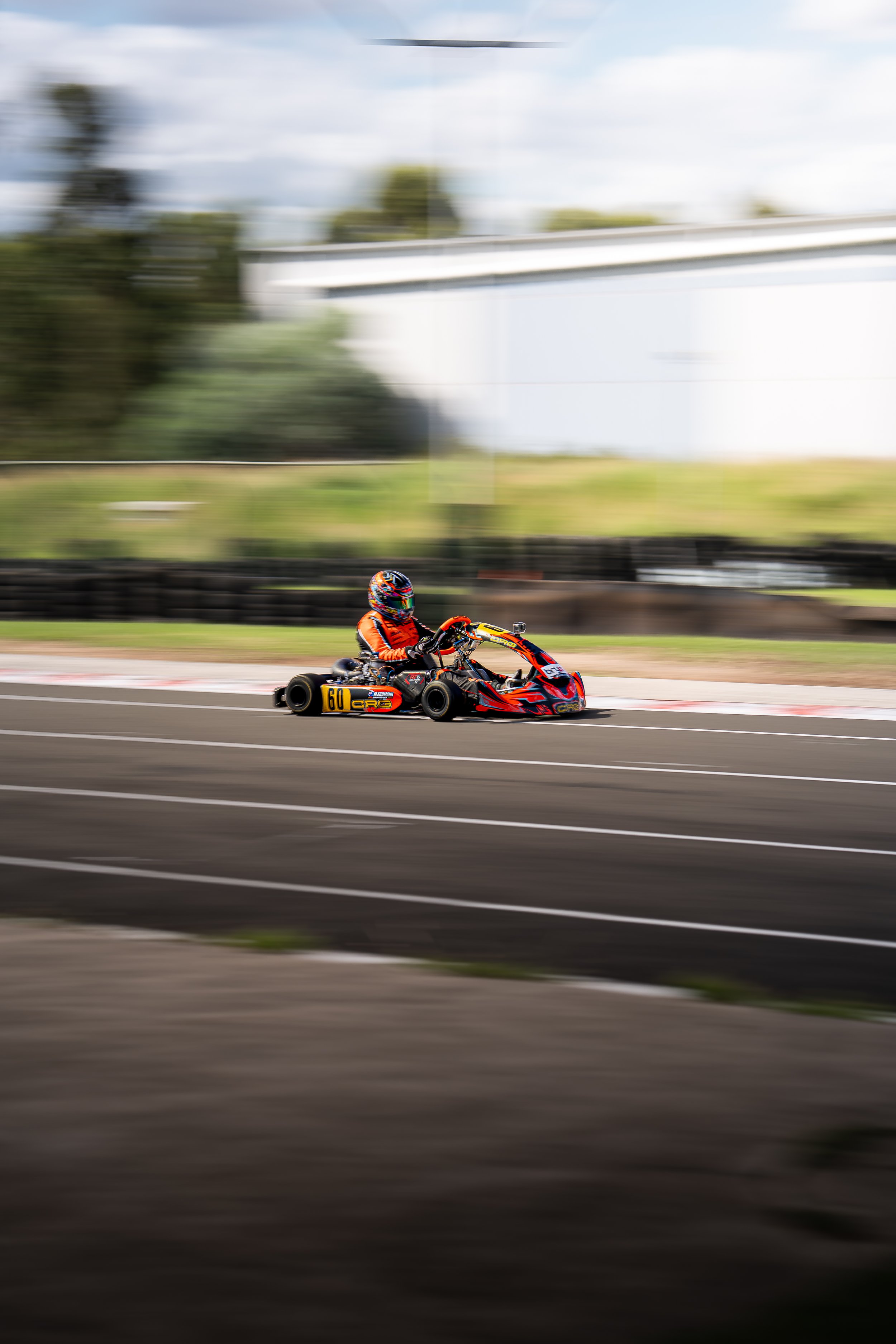 A person in racing gear driving a go-kart on a race track, with motion blur background.