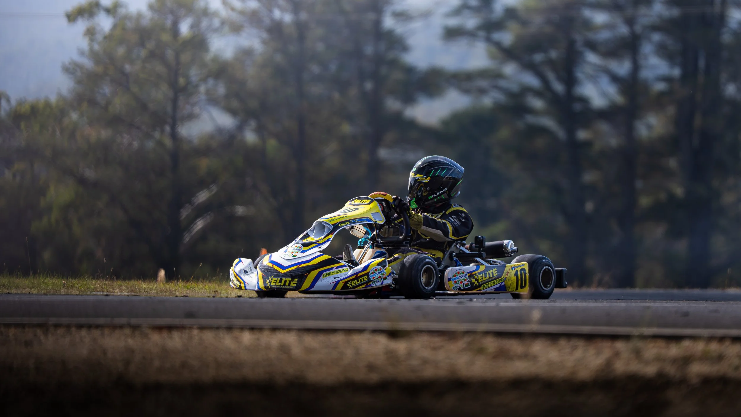 A person riding a go-kart on a track with trees in the background during daytime.