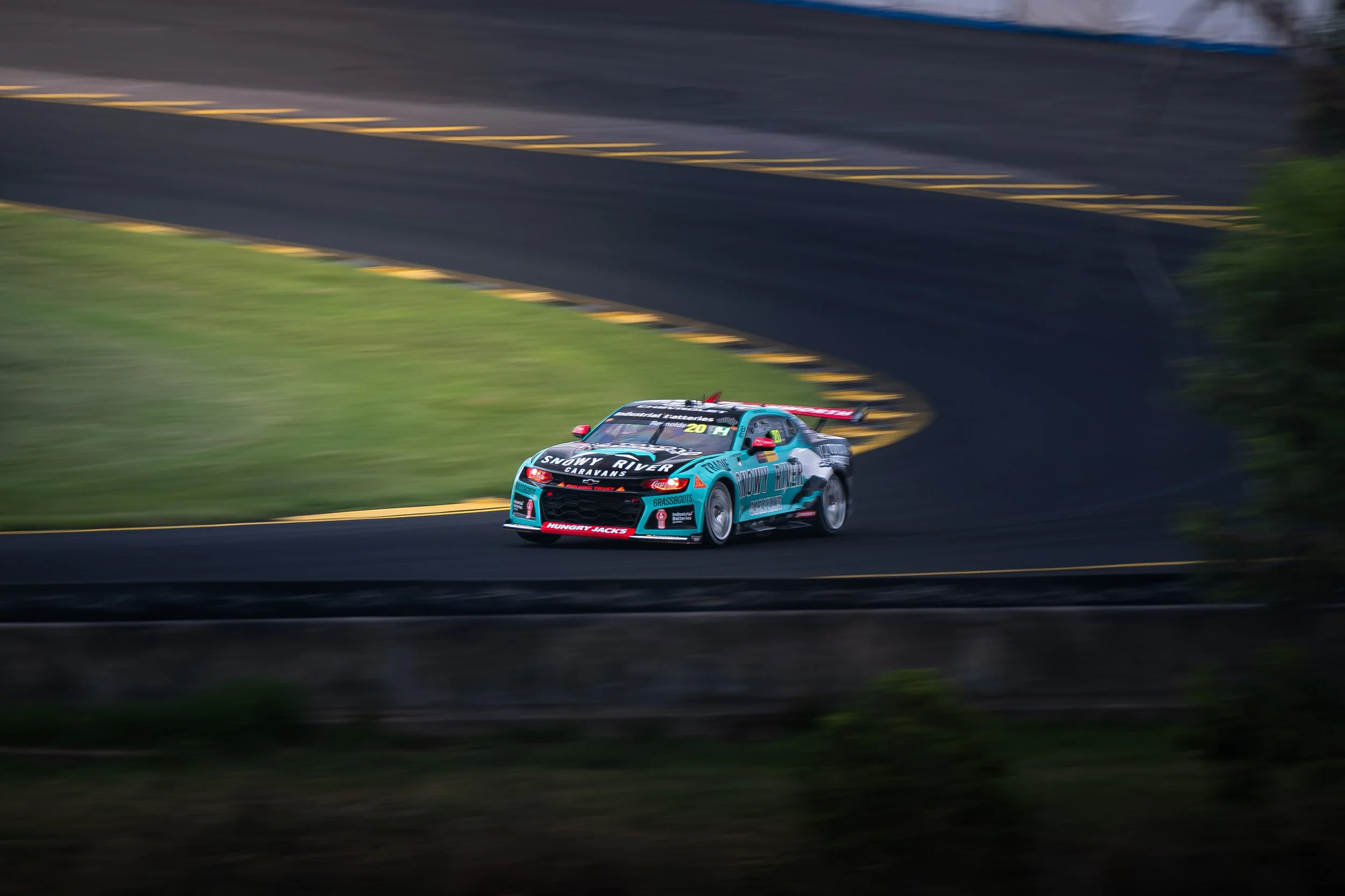 A brightly colored race car moving quickly on a paved racing track with blurred background, suggesting high speed.