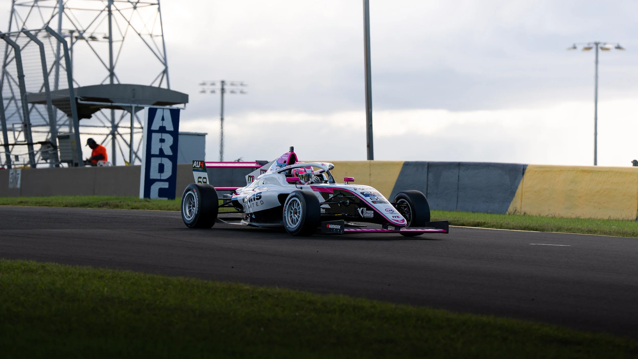 A race car with pink and white colors on a race track during daytime.