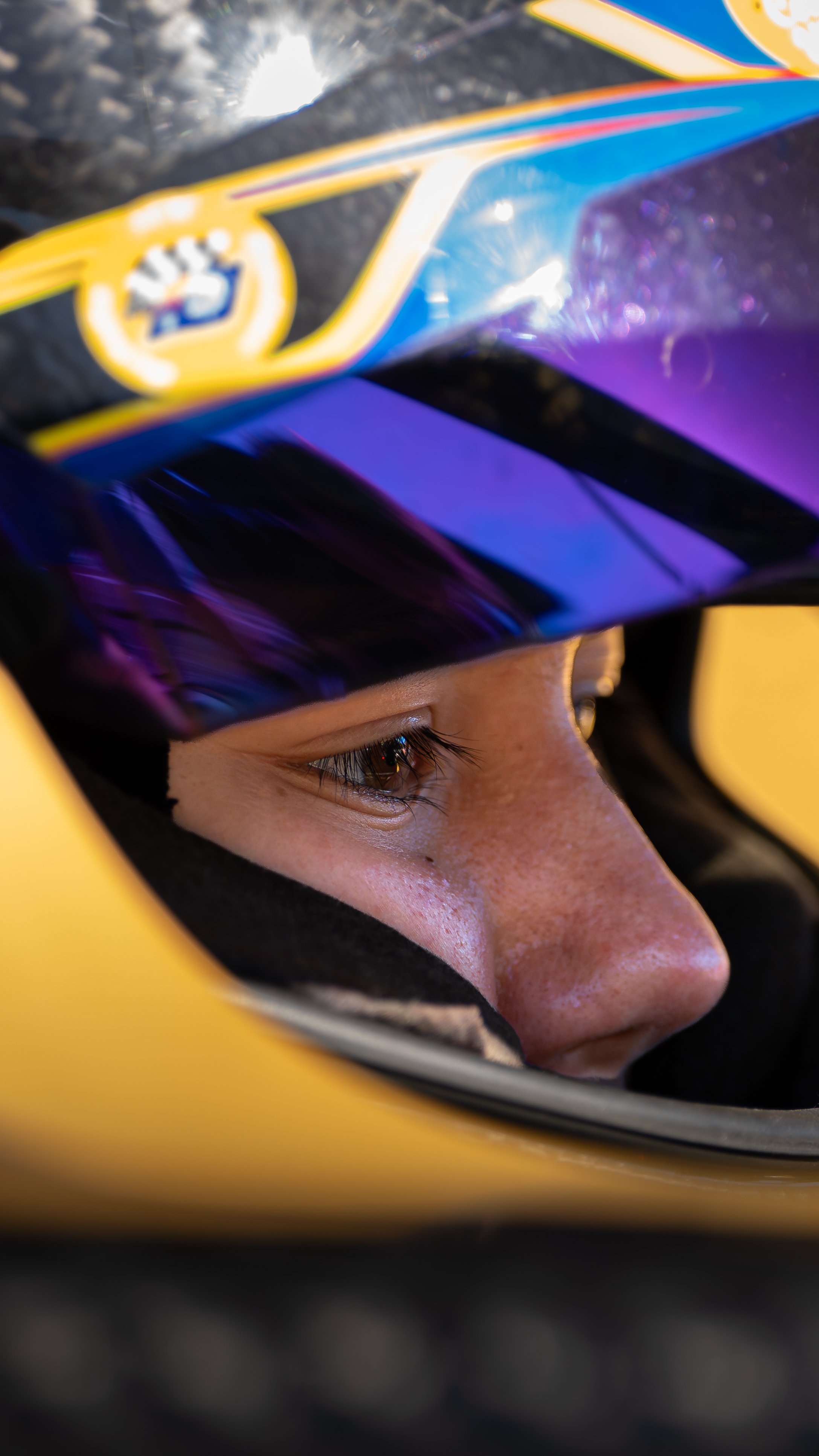 Close-up of a person's face wearing a racing helmet, focusing on the right eye with the helmet visor partially lifted.