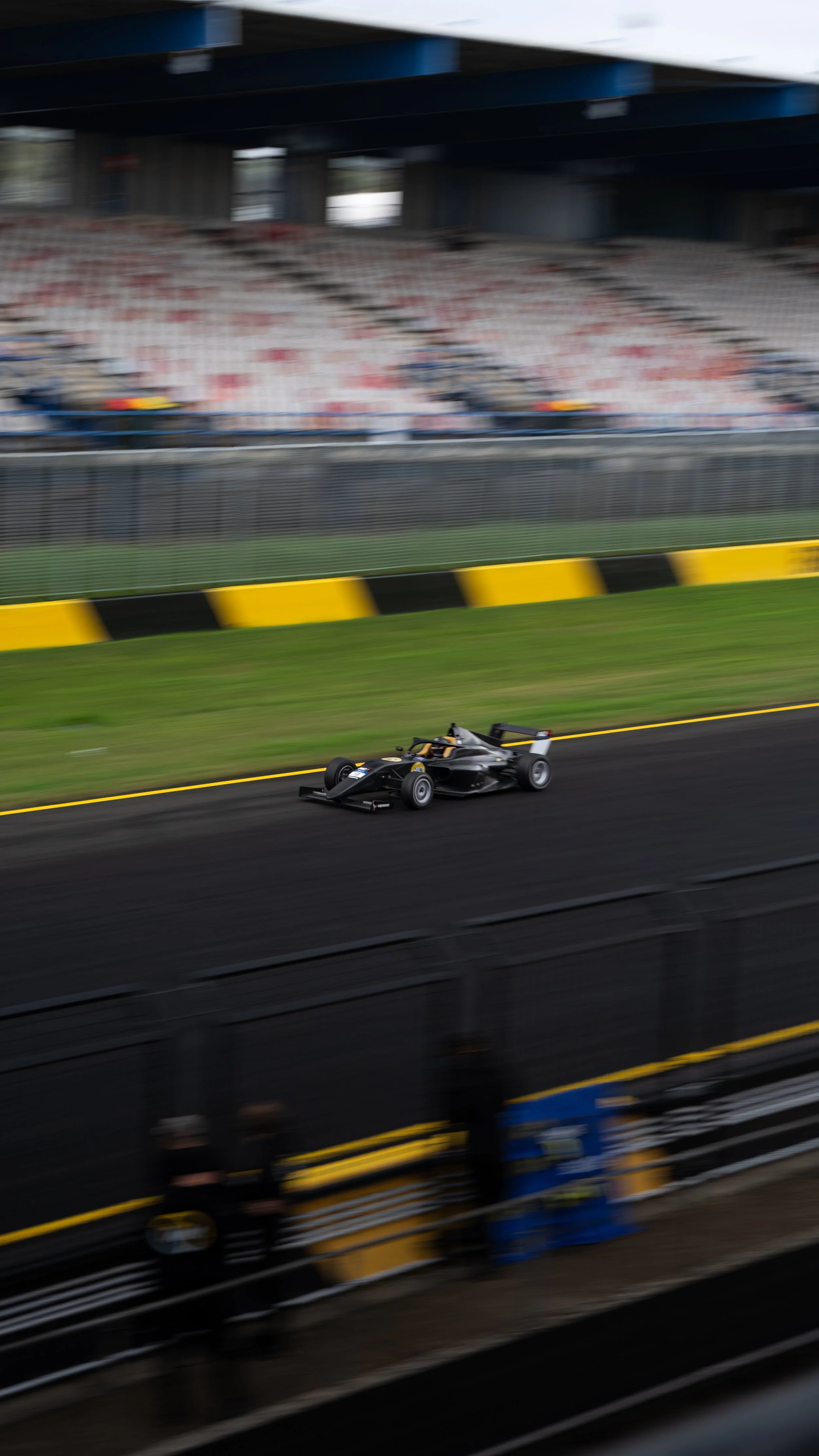 A black race car on a racetrack with grandstands in the background, appearing blurred due to its high speed.