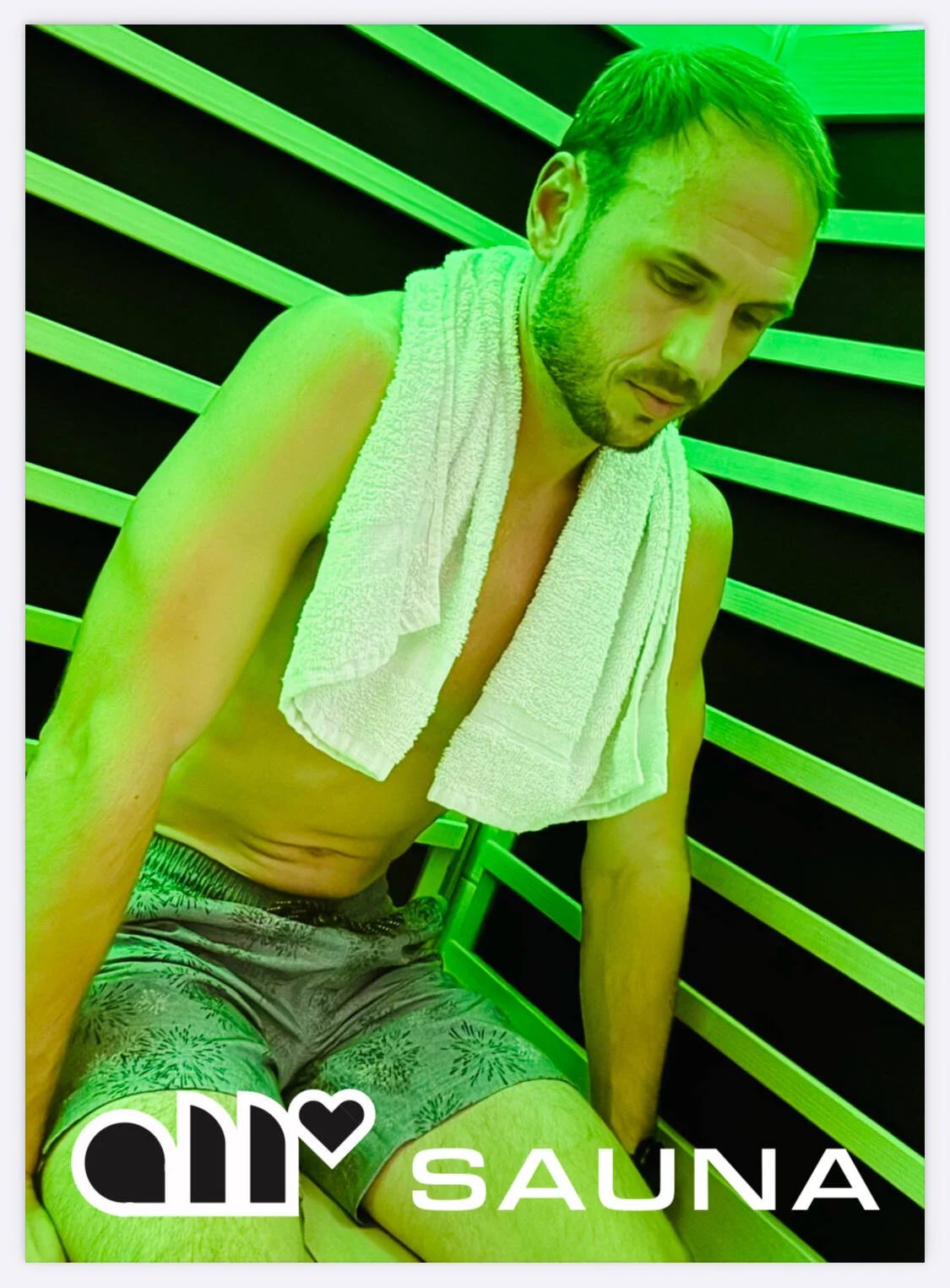 A man sitting in a sauna with wooden slats on the wall, wearing shorts, a towel over his shoulders, with green lighting, and the words ‘SAUNA’ and ‘dmp’ with a heart symbol in the lower left corner.