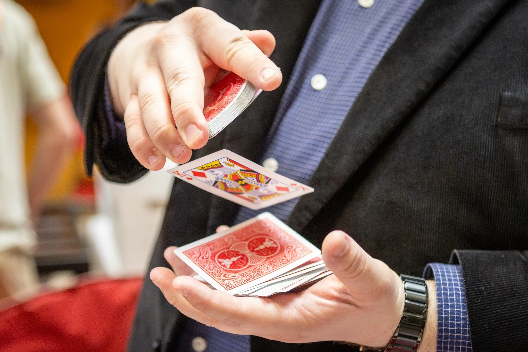 A man performs magic at an intimate gathering in a walkaround style (strolling) while holding a deck of red-backed playing cards. He performs astonishing close up magic to a small group of people including mentalism, coins, and card tricks. 