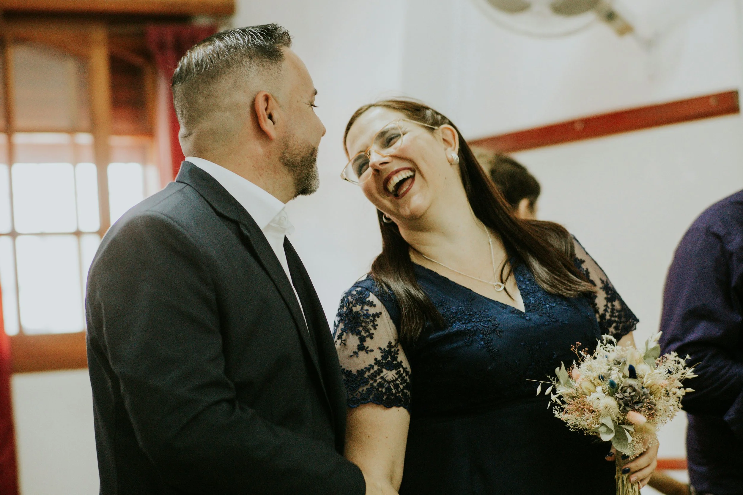 A bride and groom smiling and laughing with each other after seeing an amazing wedding magician and his performance.  The setting is private and exclusive as they share a special moment of magic together.