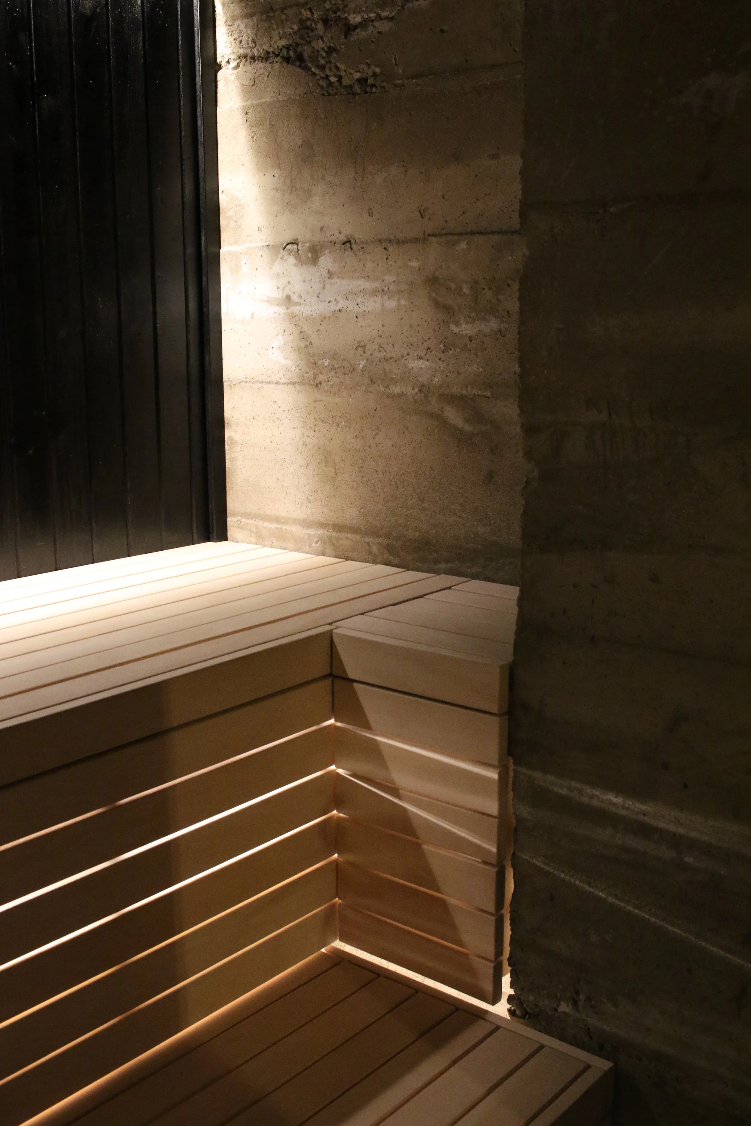 Inside a modern sauna with wooden benches, concrete walls, and subtle lighting.