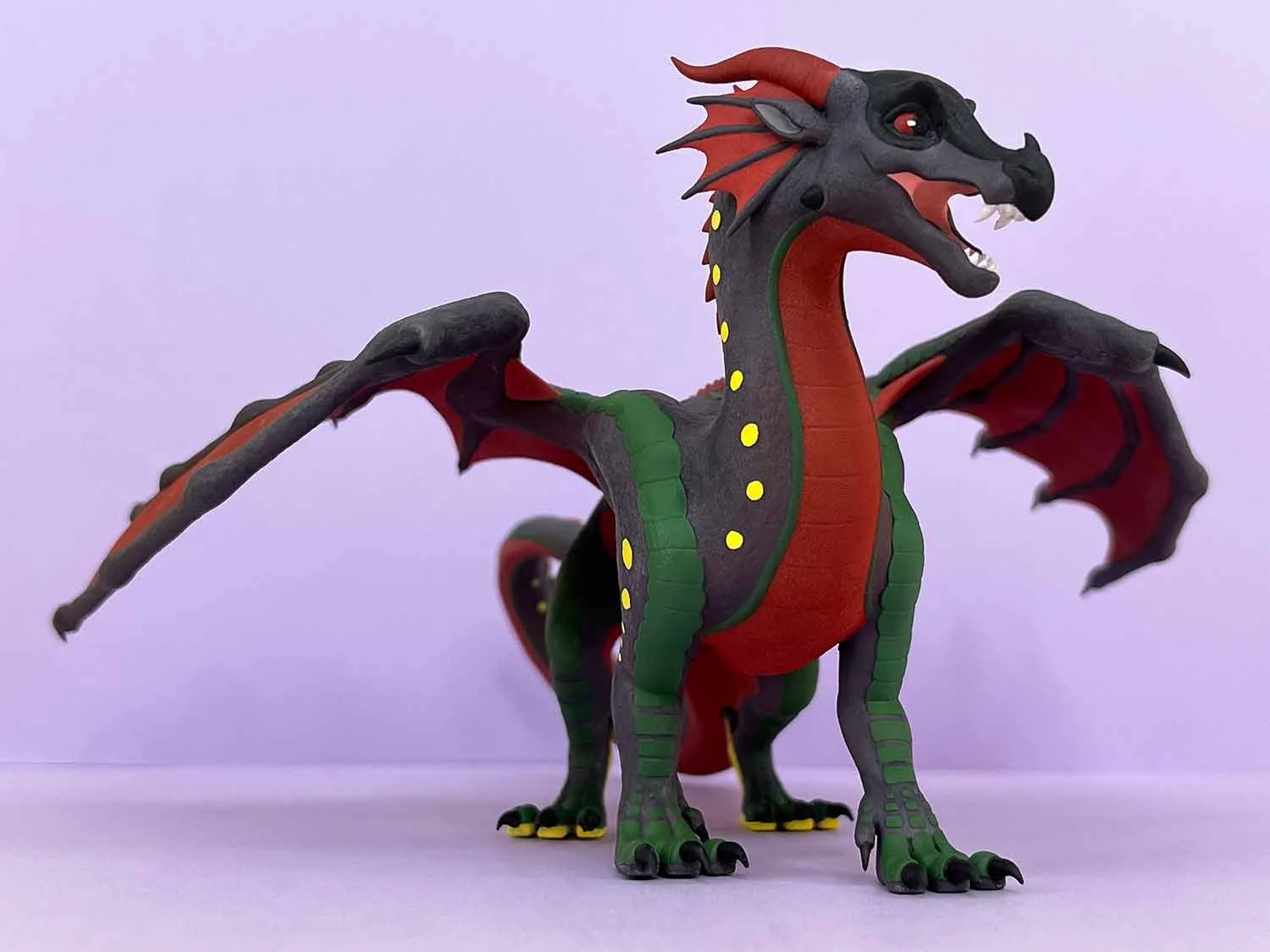 Colorful dragon figure with red, black, green, and yellow details standing on a light pink surface with a light pink background.