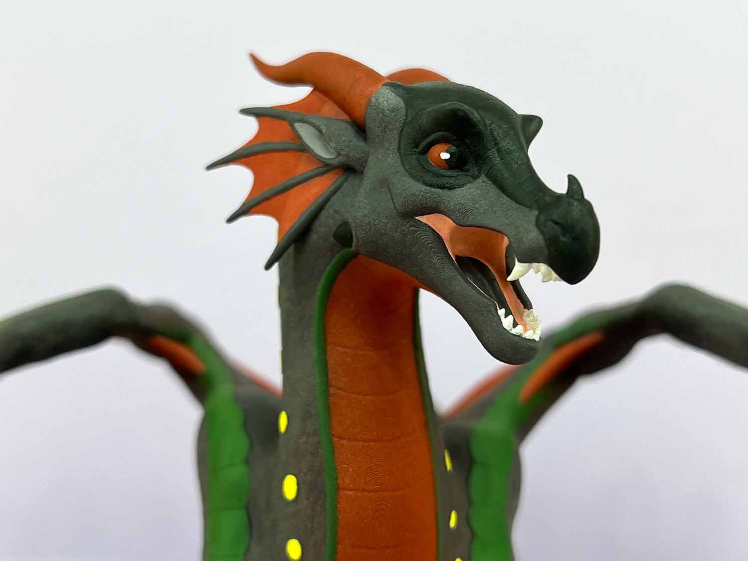 Close-up of a dragon figurine with gray, red, and green colors, showing detailed facial features and open mouth with visible teeth.