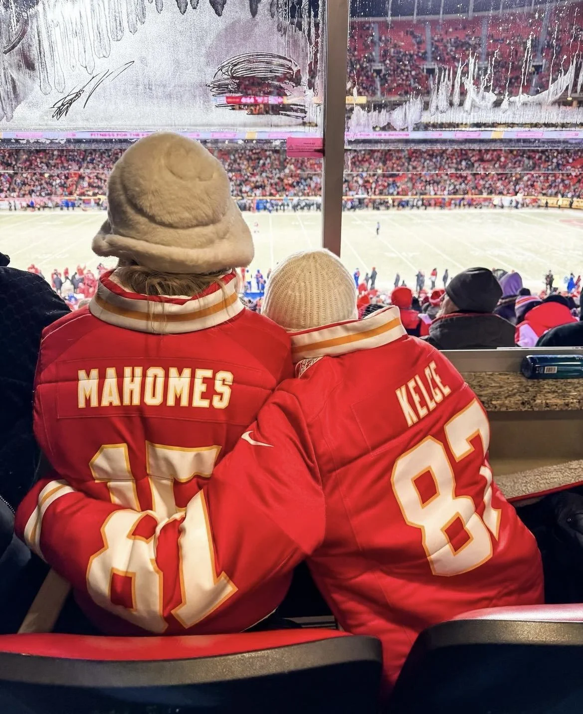 Two fans in red Kansas City Chiefs jerseys sitting in a stadium, with one wearing the Reddi-Wip Dollop Hat