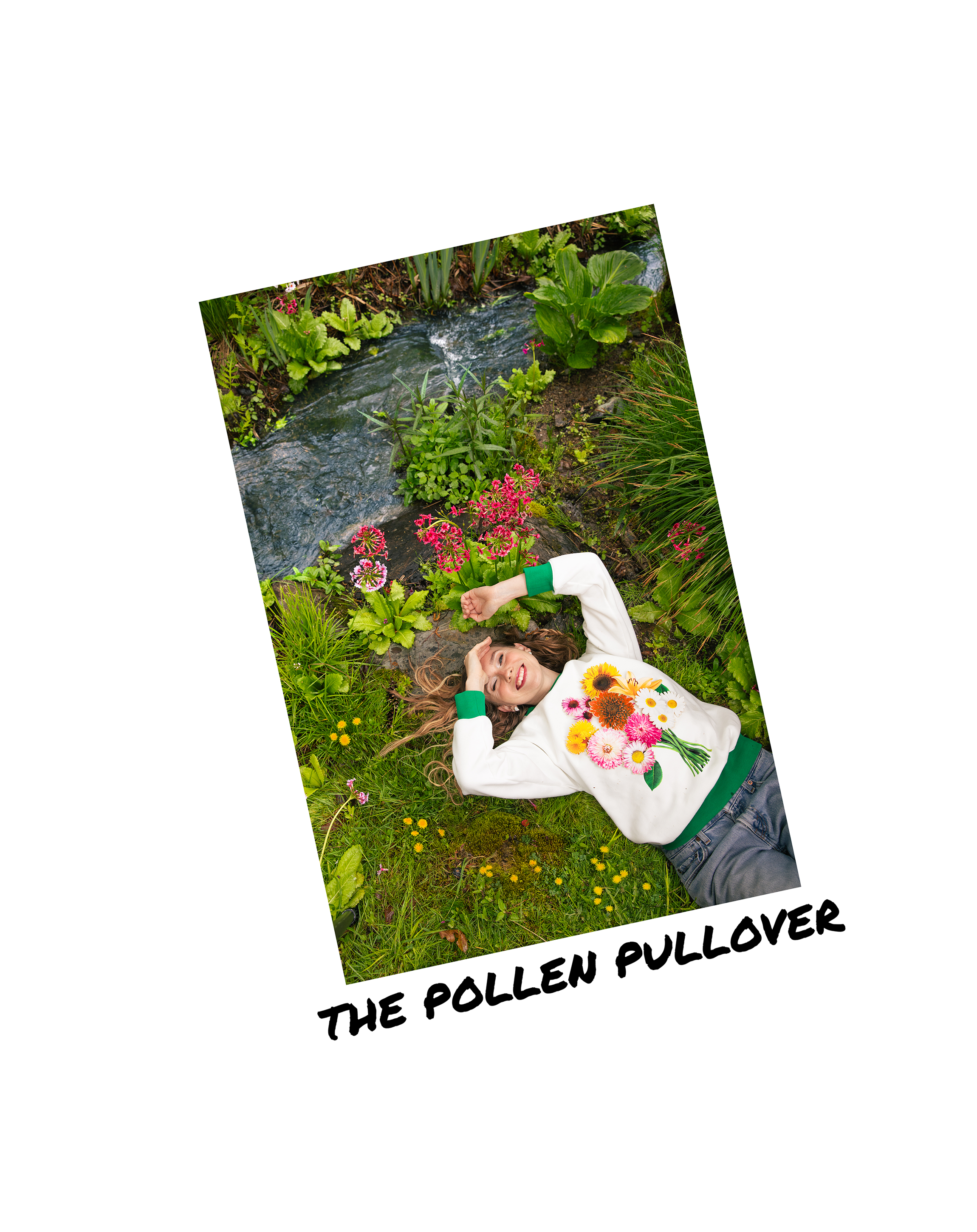 Young woman lying on grass in a garden, smiling, holding a bouquet of colorful flowers, with lush green plants and a small stream in the background.