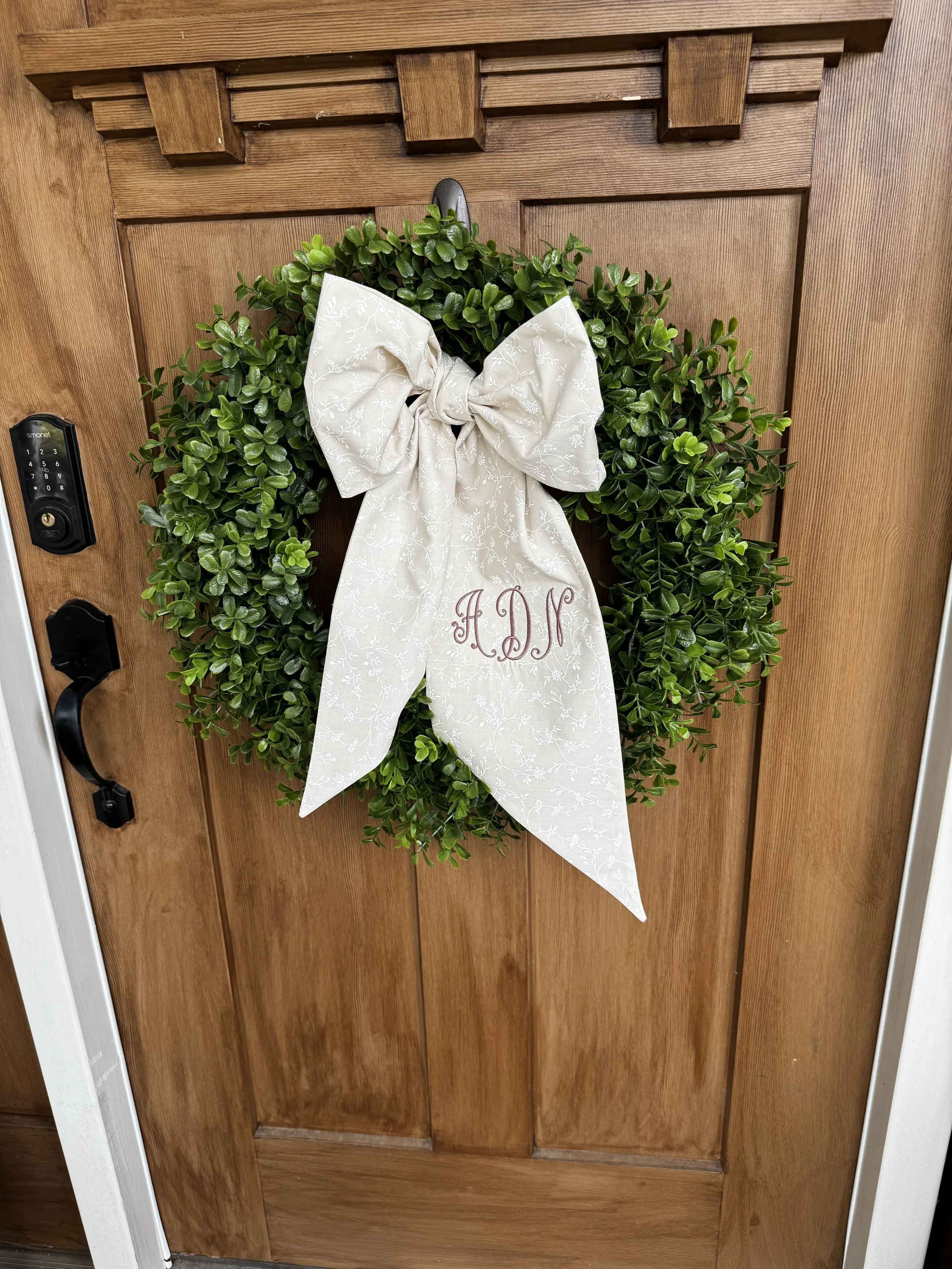 Personalized monogrammed wreath bow displayed on a green wreath on a wooden front door. (Copy)