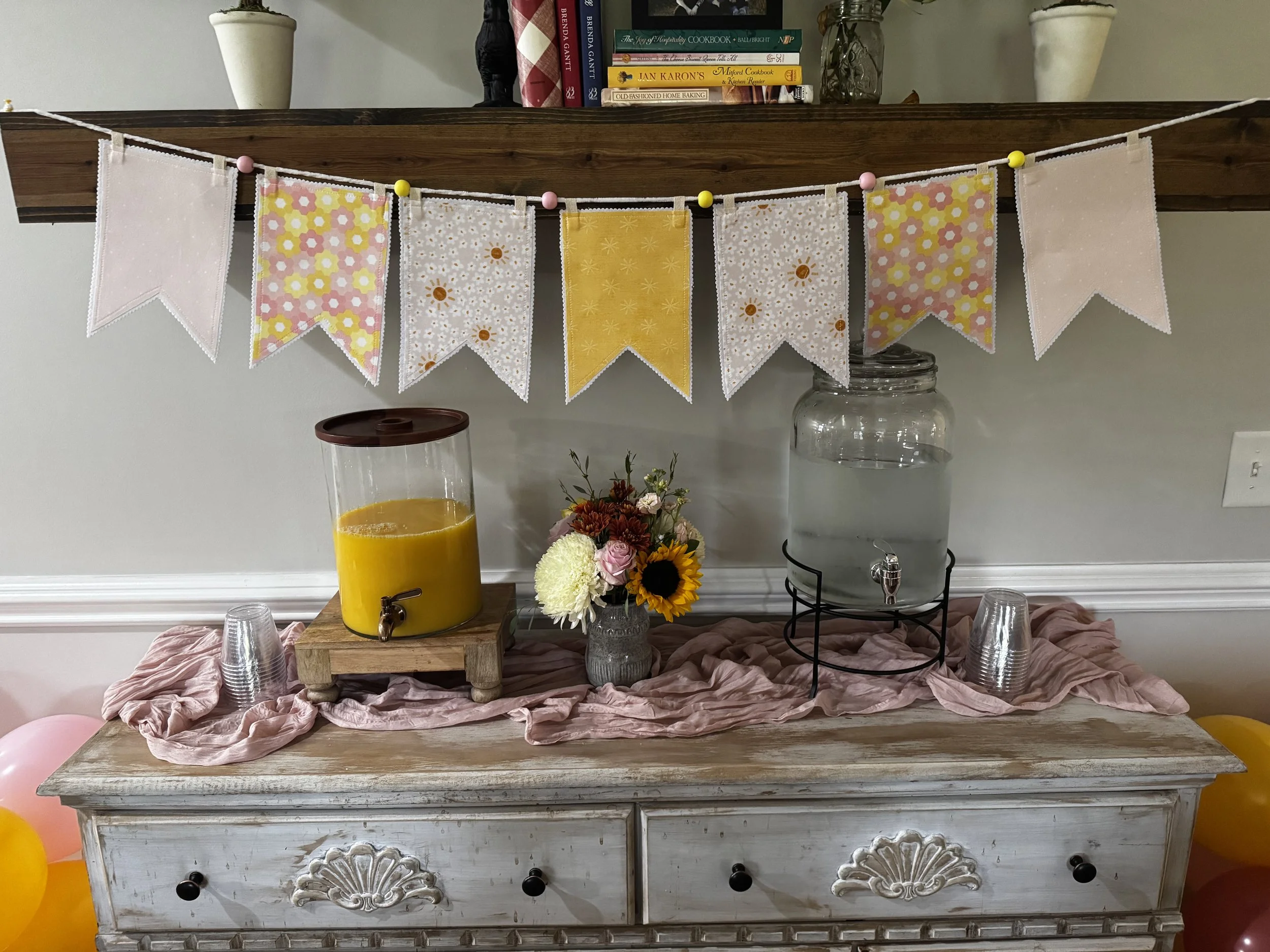 Handmade fabric pennant garland in coordinating yellow, pink and floral cotton prints displayed above a decorated party table.