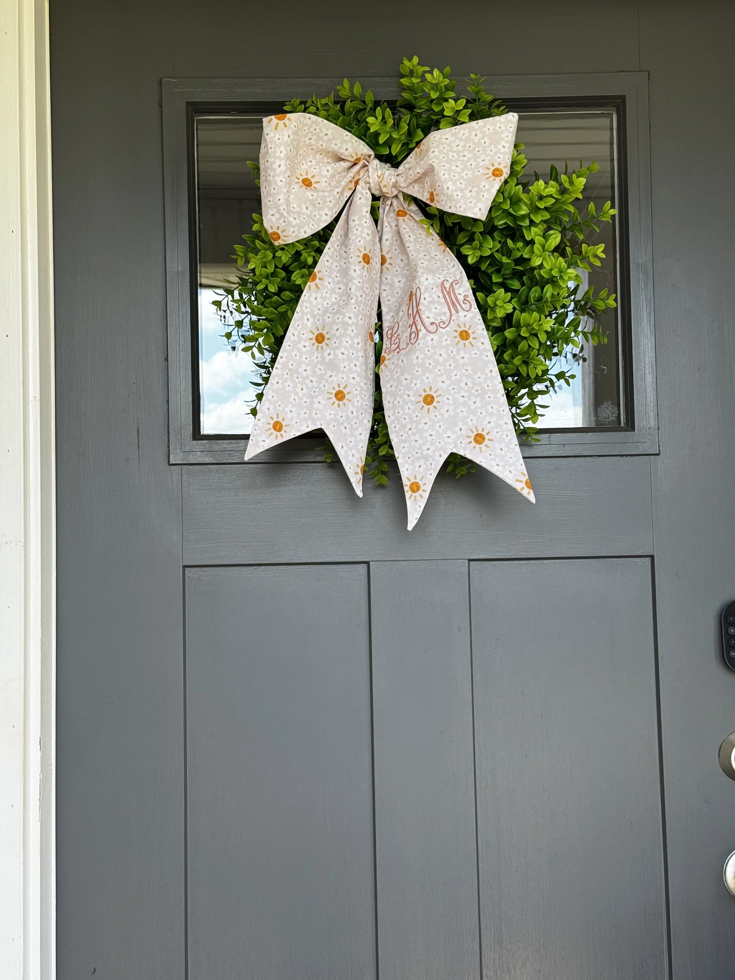 Personalized fabric wreath bow displayed on greenery on a front door. (Copy)