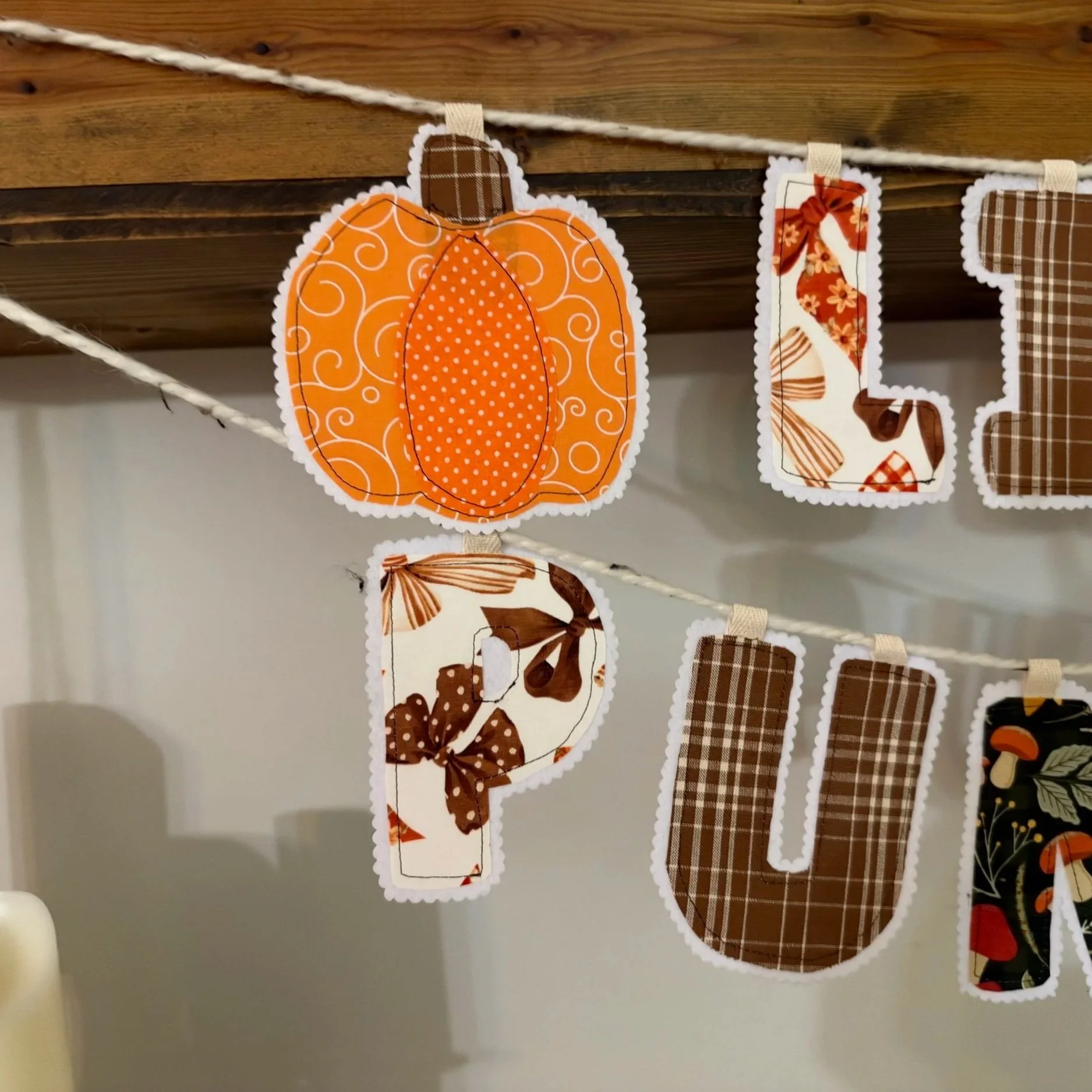 Handmade orange pumpkin fabric banner accent with decorative stitching and white scalloped felt backing, displayed with a fall letter garland.