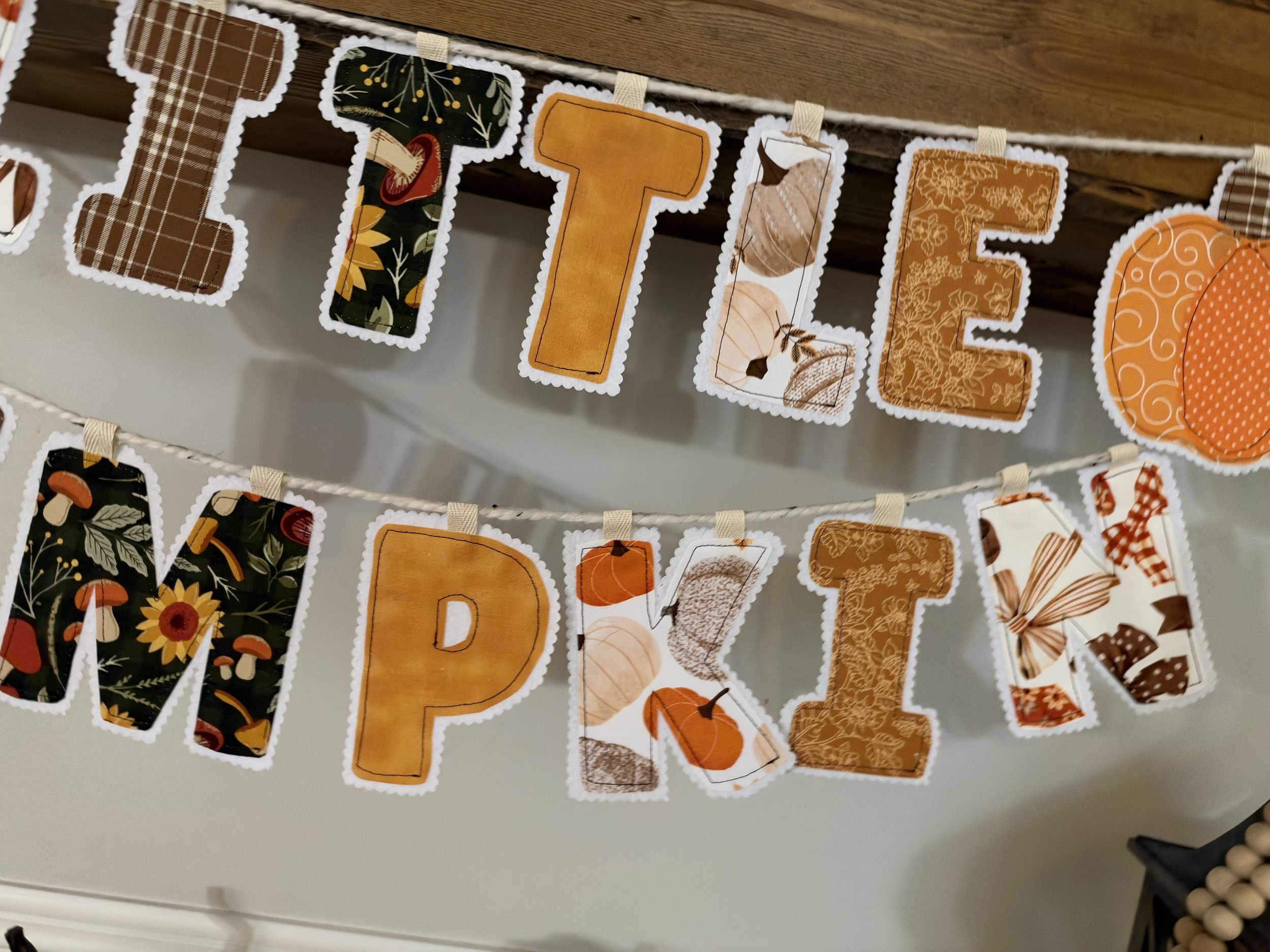 Close-up of handmade Little Pumpkin banner letters with orange fall fabrics, decorative stitching and felt backing.