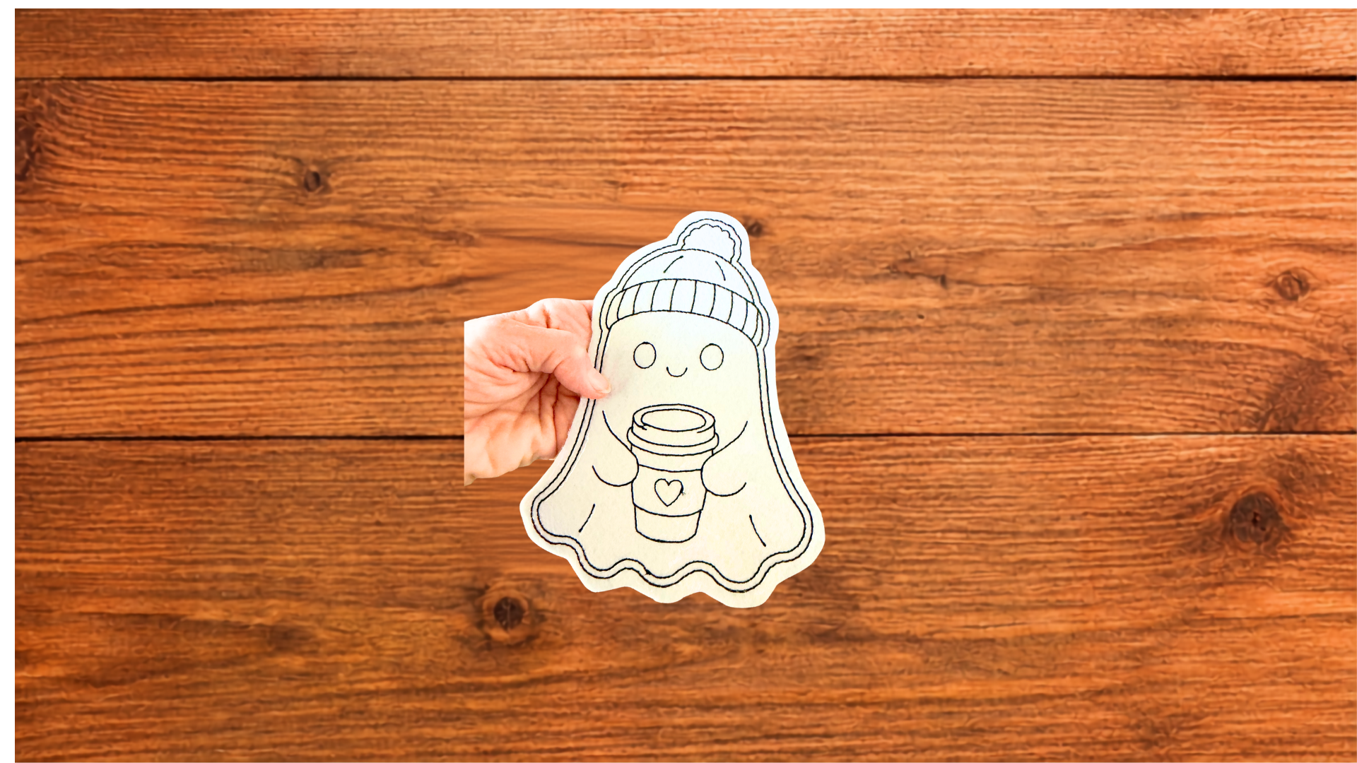 Cozy Coffee Ghost Reusable ghost Coloring Cutie wearing a pom-pom hat and holding a coffee cup, shown against a wooden background. (Copy)