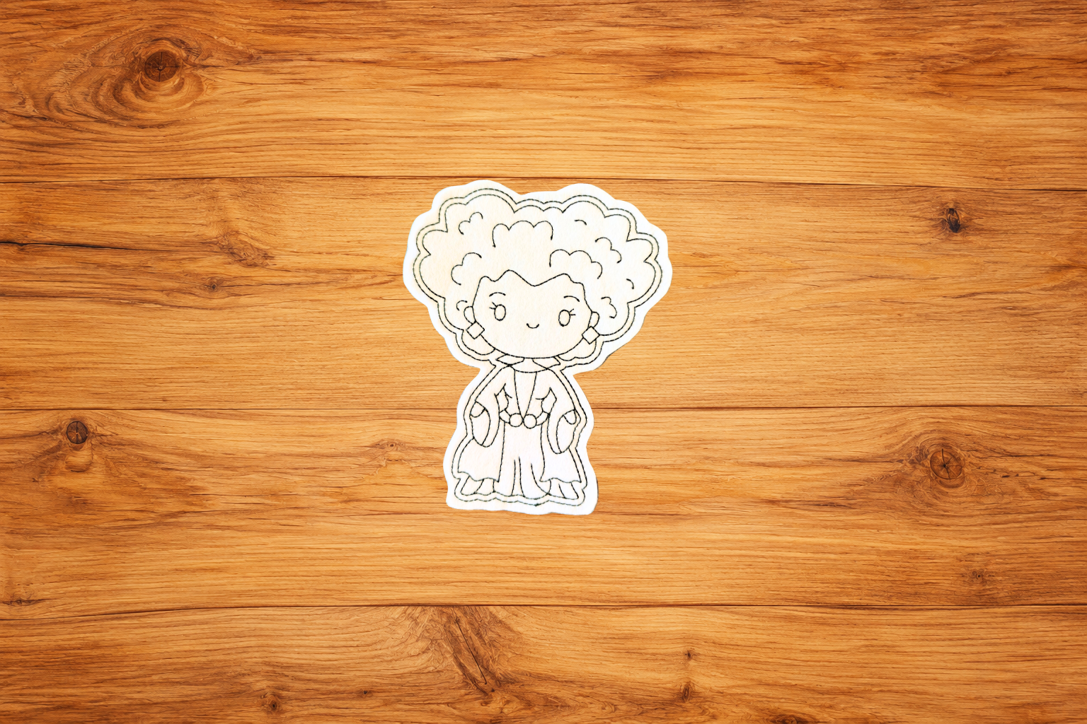 Handmade Witchy Woman Coloring Cutie with curly hair and embroidered outlines on a warm wood background