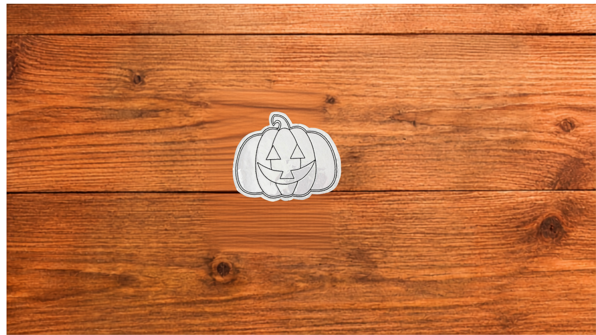 Reusable Jack-o'-Lantern Coloring Cutie with smiling pumpkin face and black stitched outlines on a wooden background. (Copy)