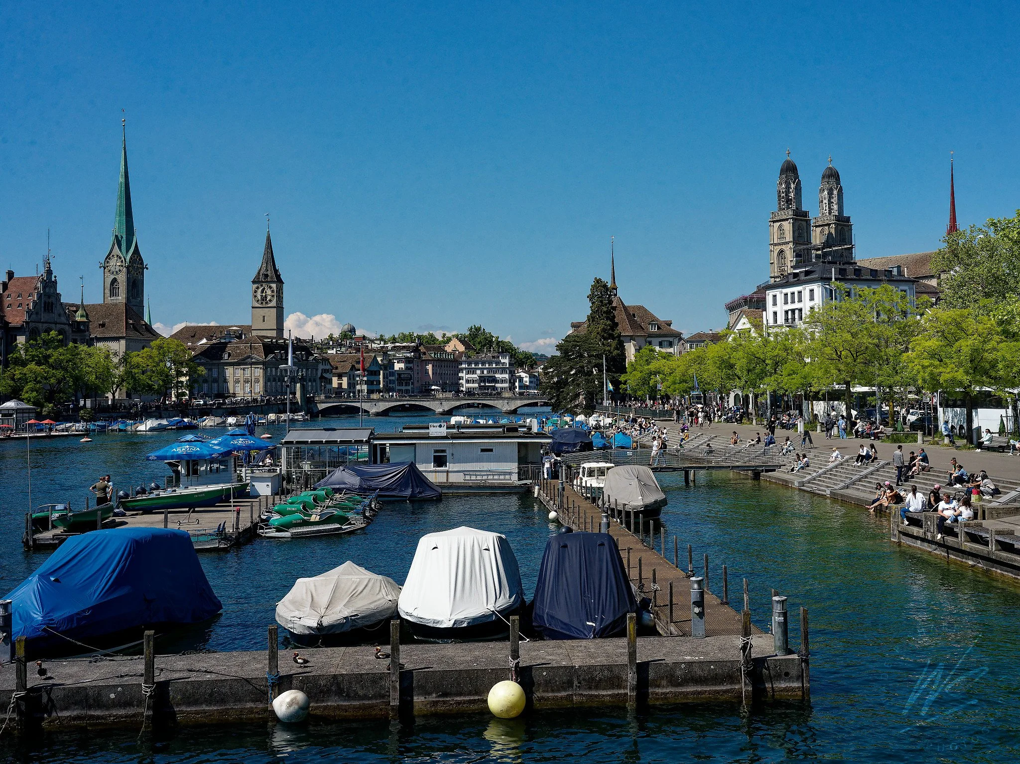 The Limmat River and Zurich Old Town skyline, Zurich, Switzerland. Left to right: the green spire of the Fraumünster, the clock tower of St. Peter's Church — home to one of the largest clock faces in Europe — and the twin Romanesque towers of the Gro