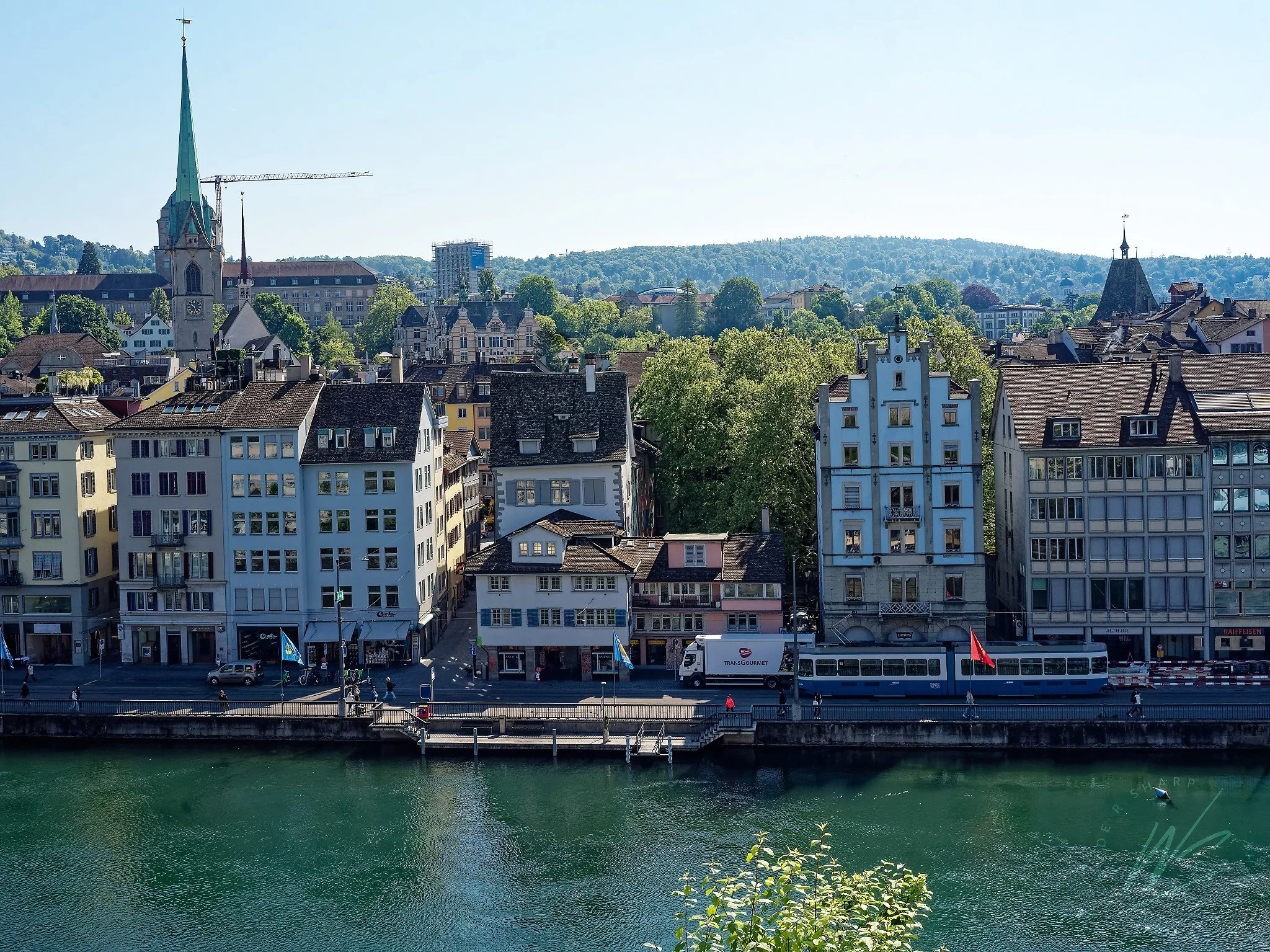 The left bank of the Limmat River and Zurich Old Town, viewed from across the river, Zurich, Switzerland. The green spire of the Fraumünster — home to the famous Marc Chagall stained glass windows — rises above the rooftops on the left, while a blue 