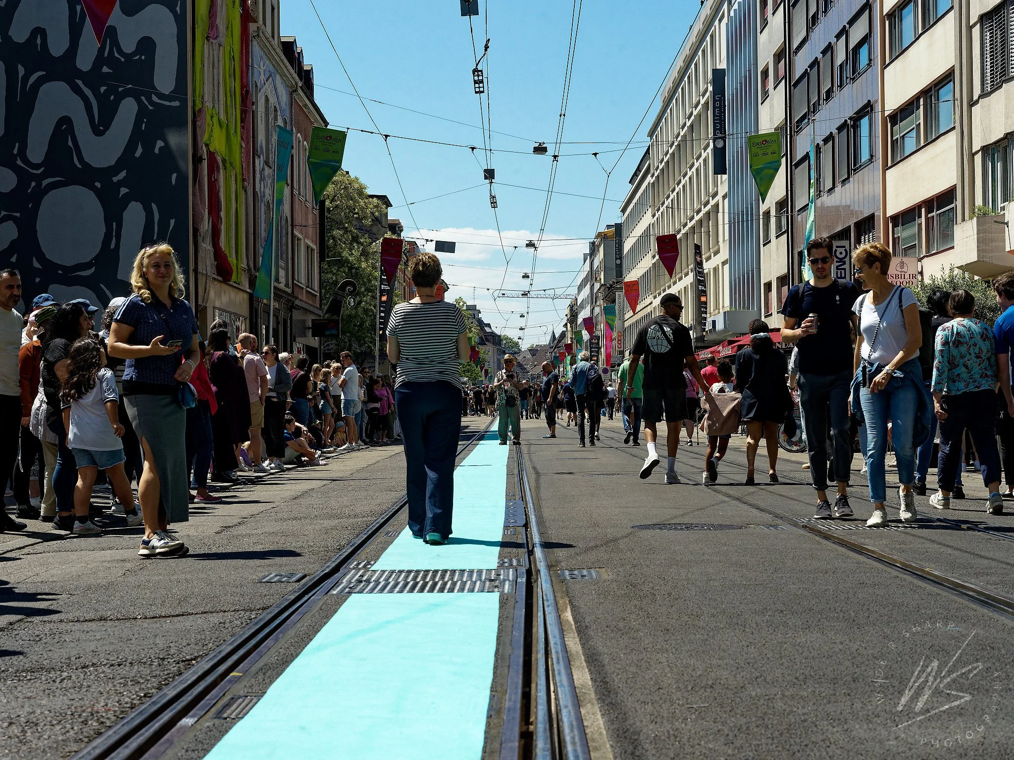 Basel city centre transformed for the Eurovision Song Contest 2025, Switzerland. Tram tracks painted turquoise — the contest's signature colour — line the pedestrianised Freie Strasse shopping street, decorated with Eurovision banners and colourful b