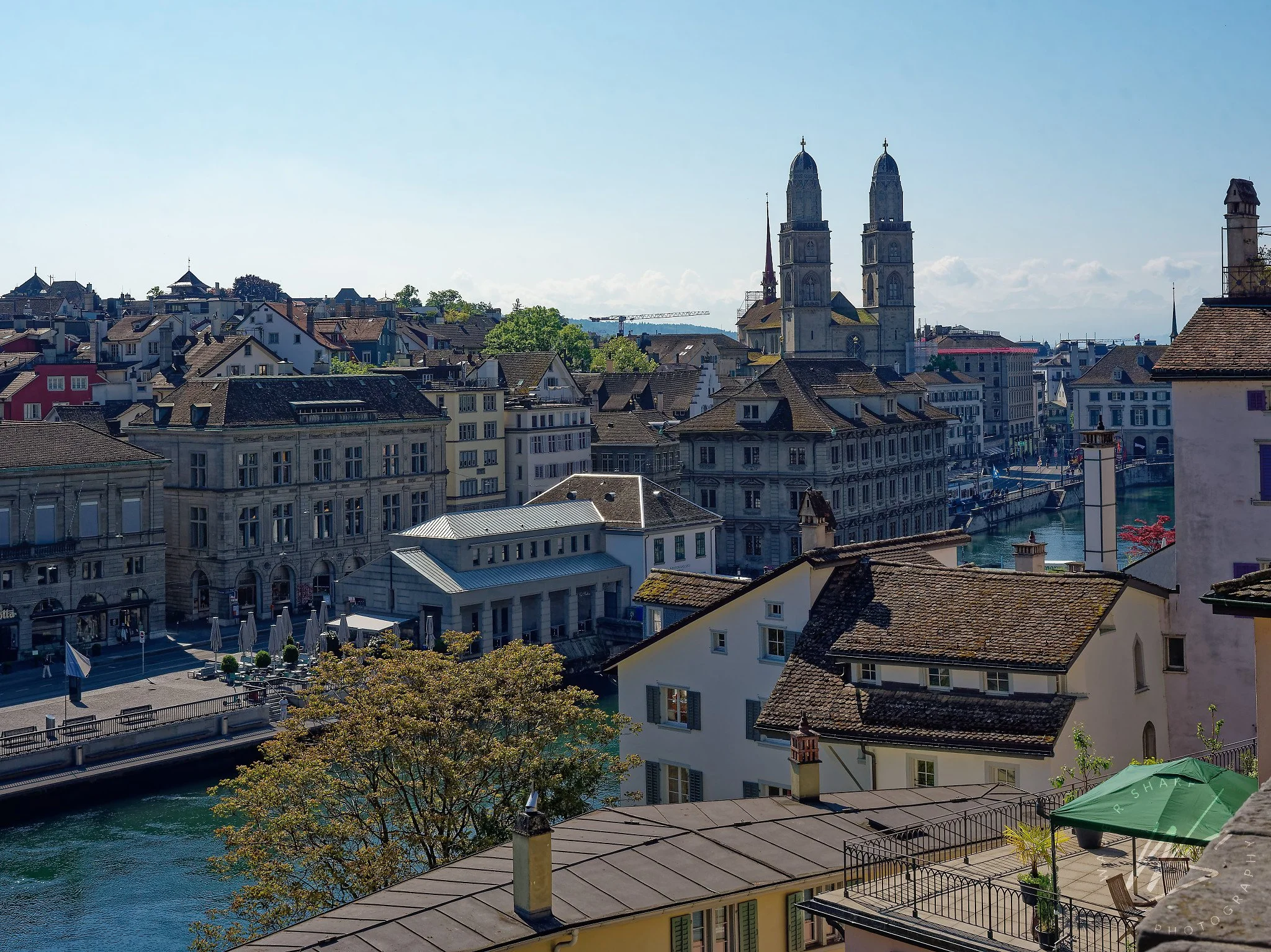 Rooftop view over Zurich Old Town looking north along the Limmat River, Zurich, Switzerland. The twin towers of the Grossmünster cathedral dominate the skyline, with the historic Limmatquai guild house waterfront stretching along the right bank below