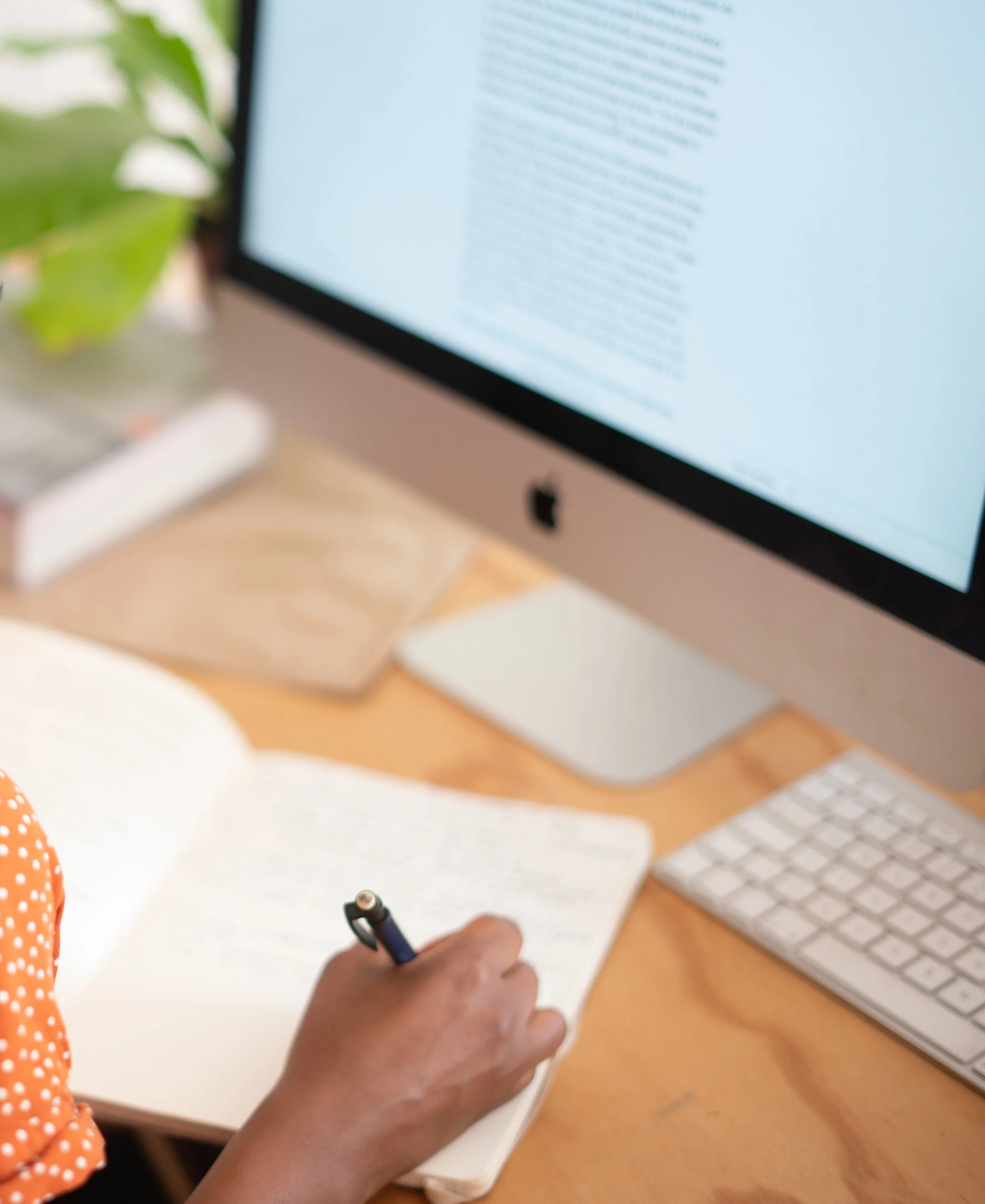 Someone writing in notebook in front of a computer