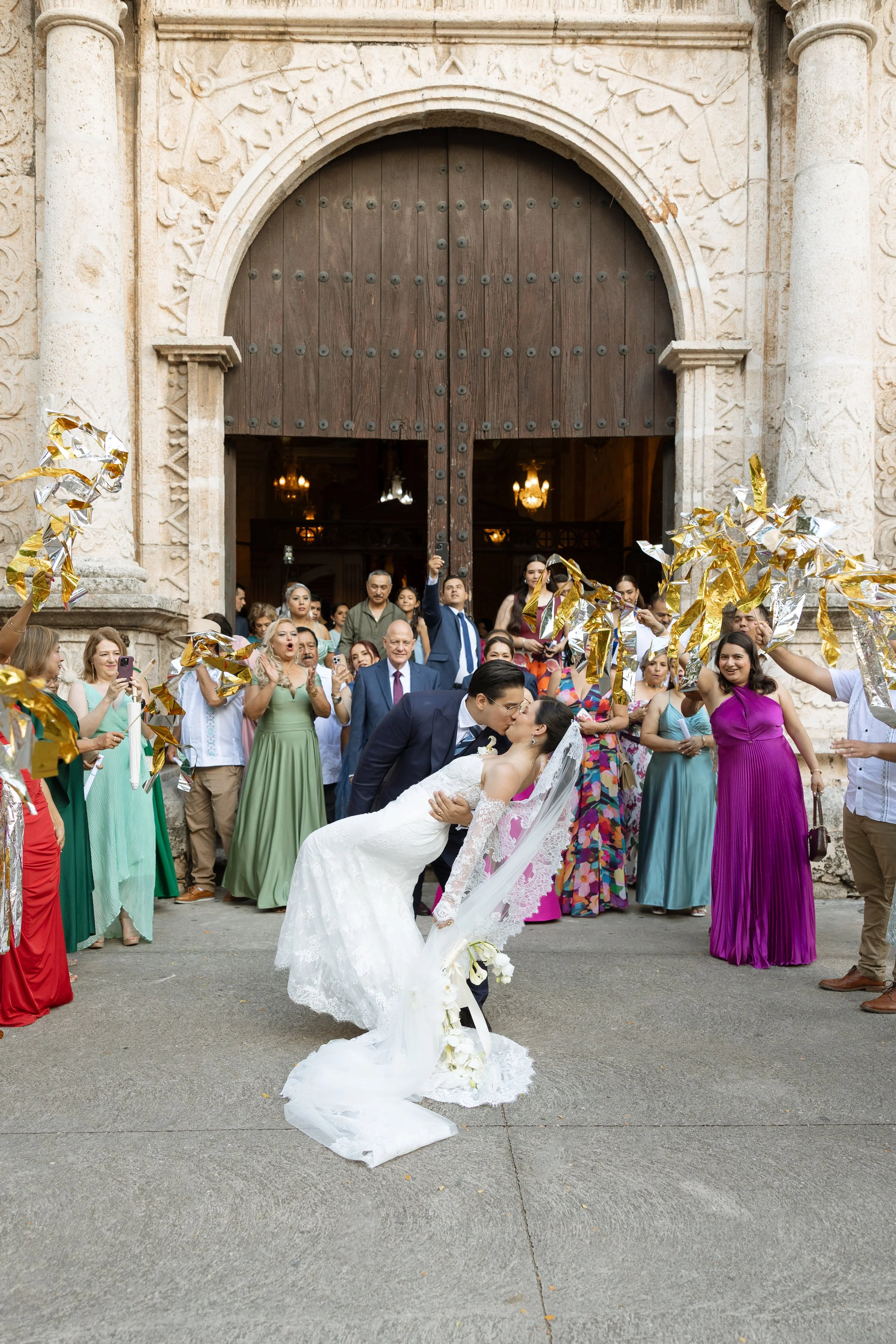 Photo of a couple kissing in front of a church and guests cheering in the background