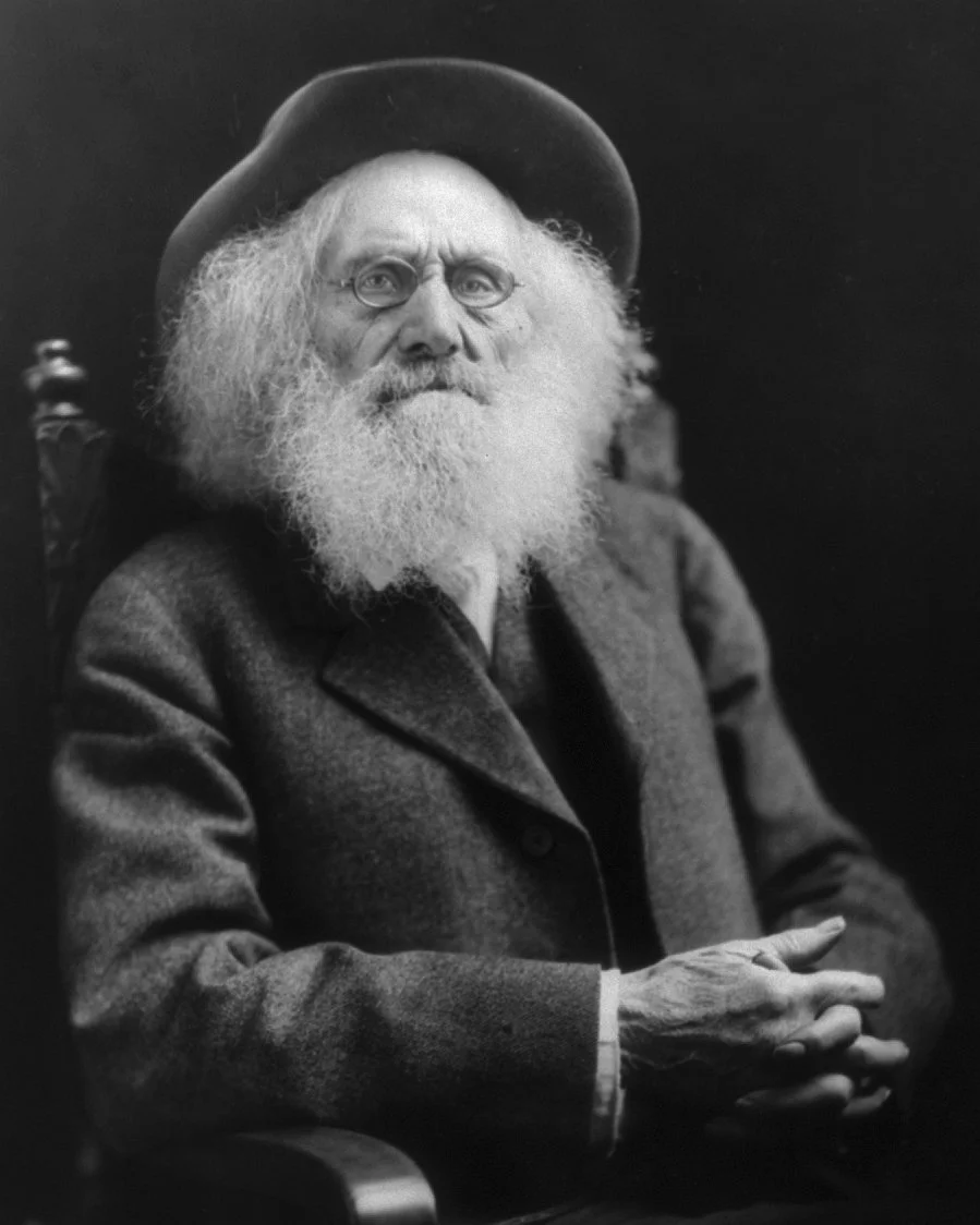 Portrait of Oregon Trail pioneer Ezra Meeker in 1921, an elderly man with a long white beard, wearing a dark coat and hat. Public domain.