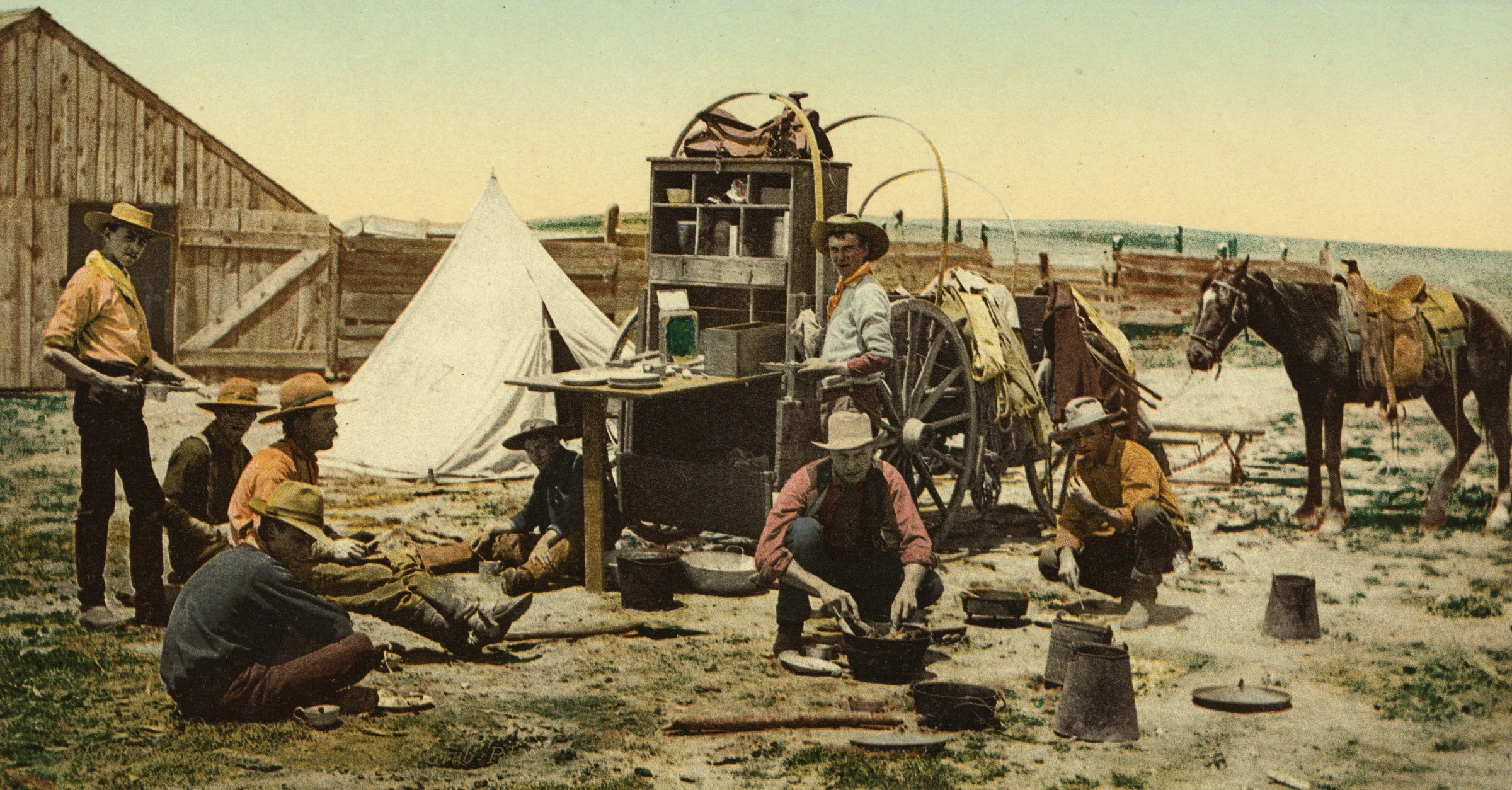 Hand-colored photochrom of a Colorado roundup camp at mealtime: cowboys sit and crouch around the cook pots and Dutch ovens by the chuck wagon, with a tent and a saddled horse behind them. Detroit Photographic Co., Library of Congress.