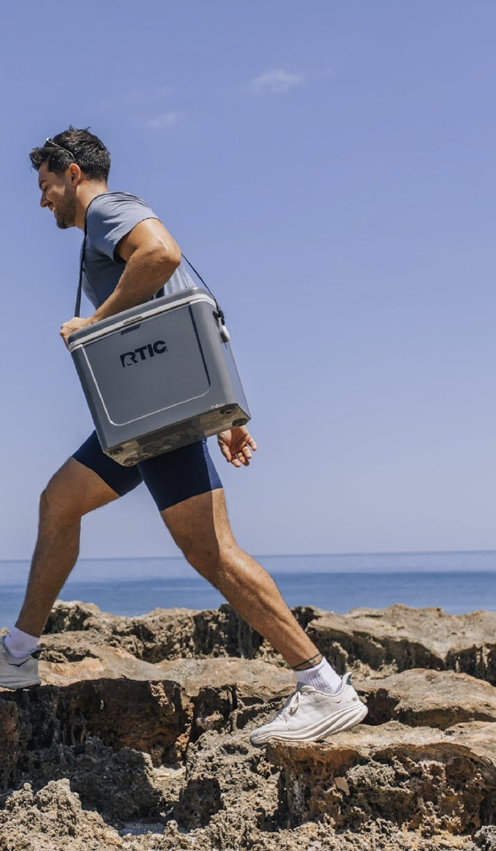 A man in athletic clothing walking on rocks near the ocean, carrying a chilled RTIC cooler over his shoulder. employee engagement, lead tracking, employee incentive, incentive program