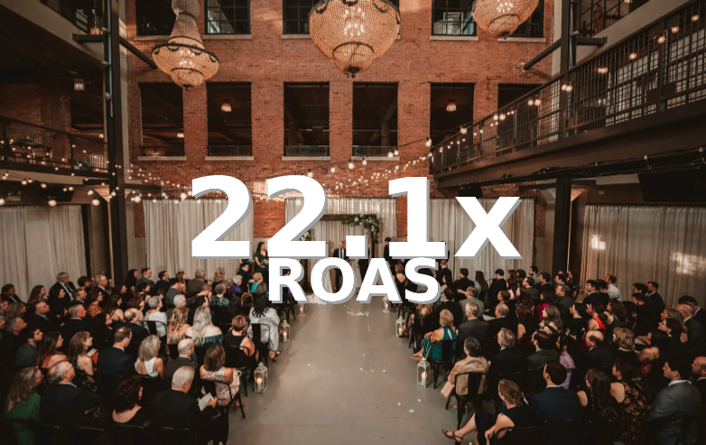 Indoor event with a large audience seated in rows, decorative hanging lights, chandeliers, and a brick wall backdrop.