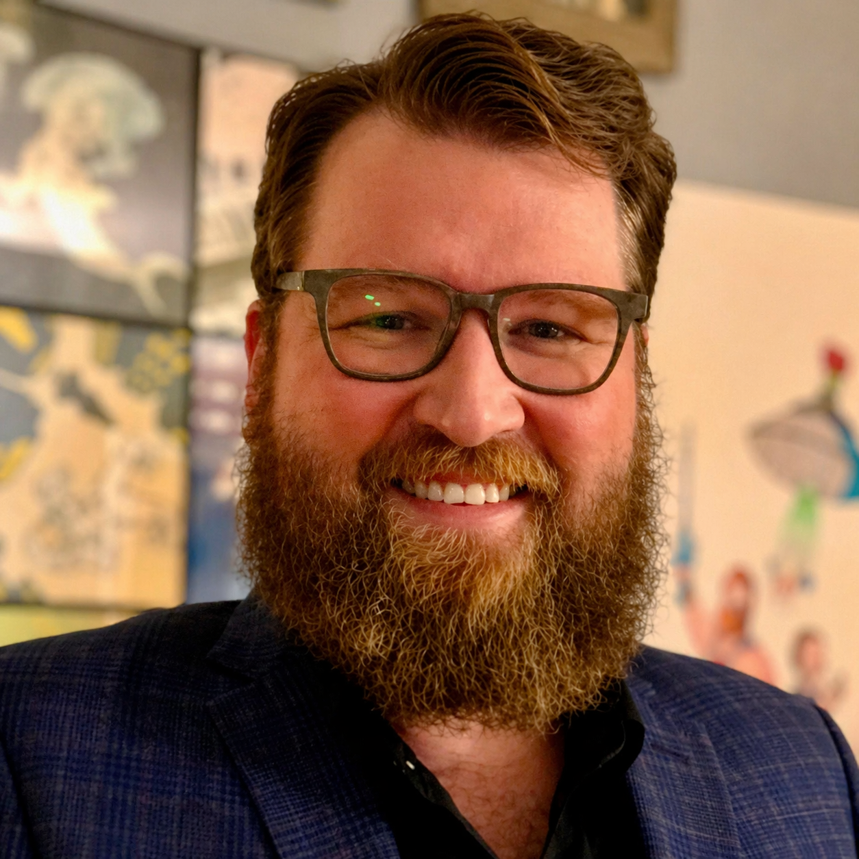 Close-up of a smiling man with glasses and a full beard in an indoor setting.