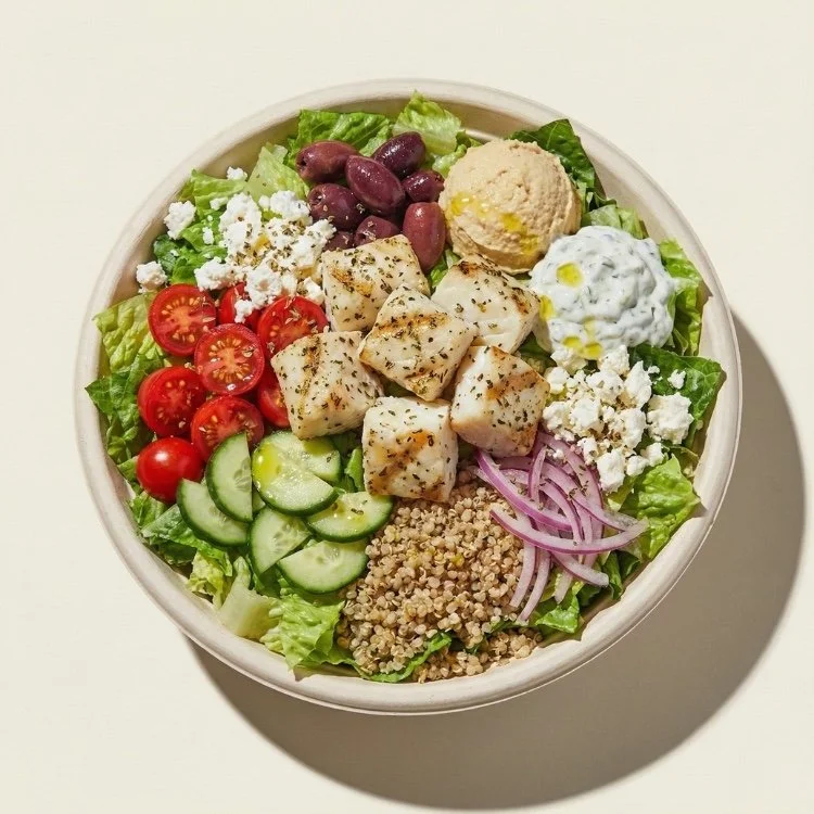 Bowl estilo mediterráneo con filete de pescado blanco a la plancha, ensalada de tomate y pepino, aceitunas y salsa de yogurt.