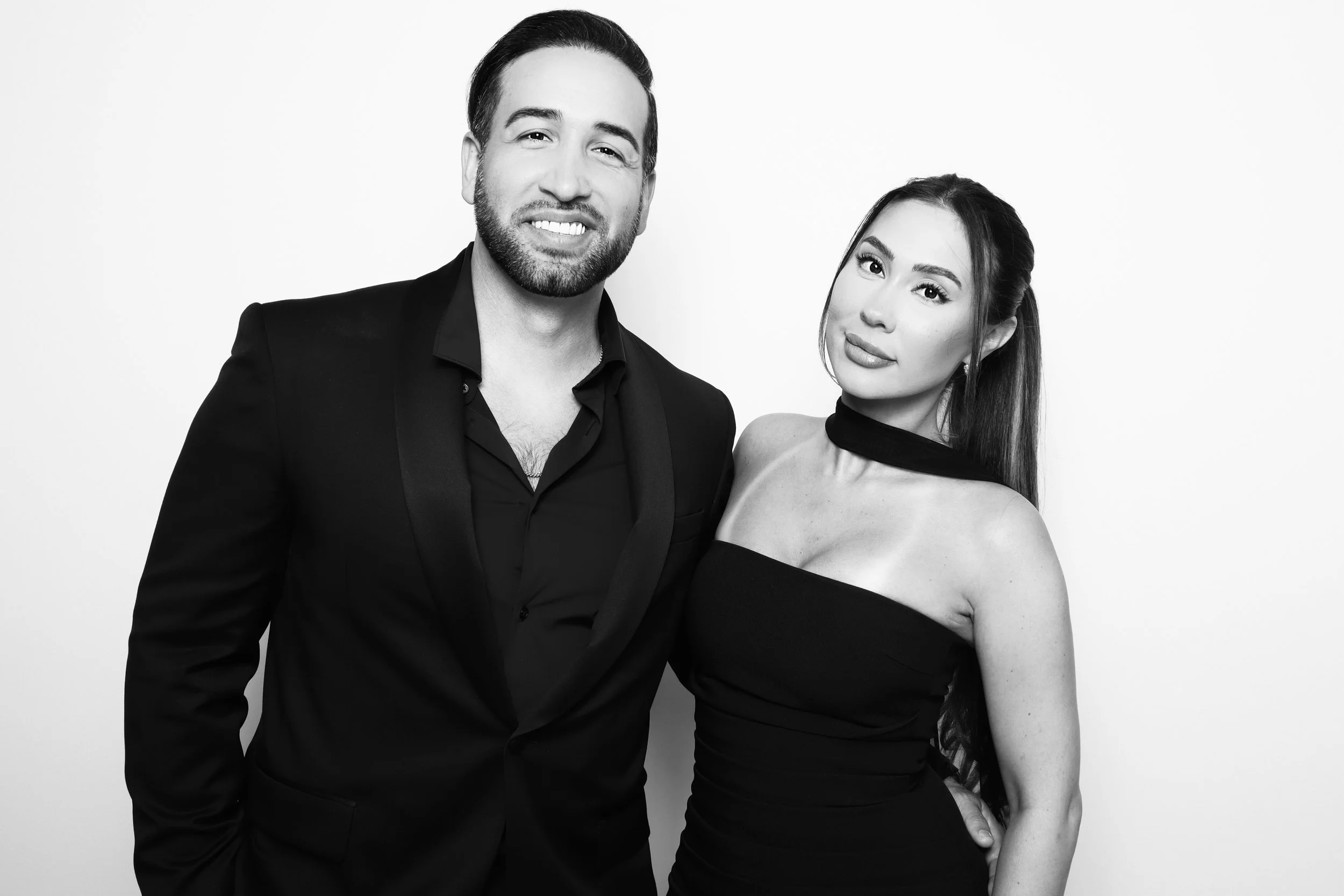 A man in a dark suit and a woman in a strapless black dress standing together and posing for a photo, black and white portrait.