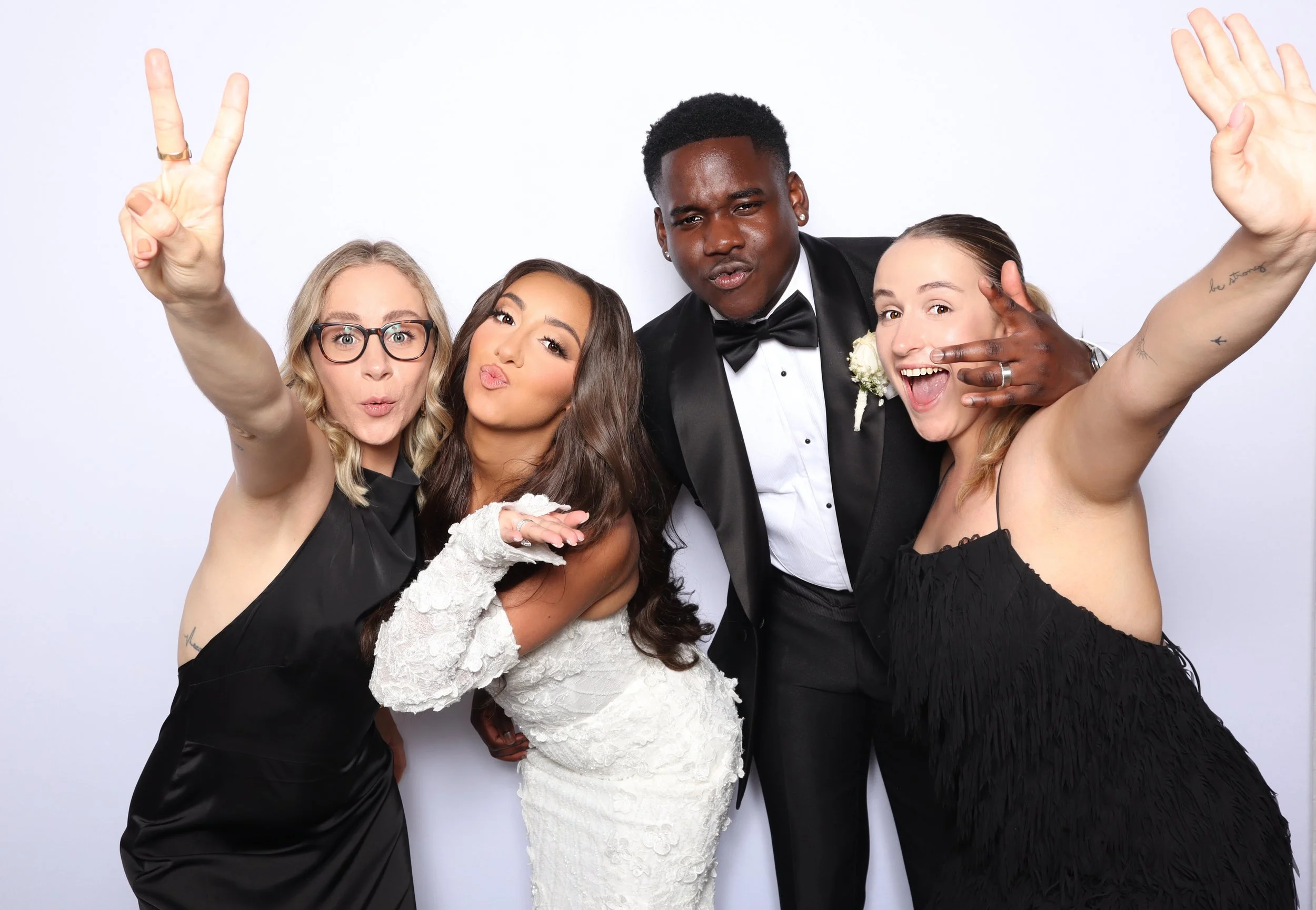 Group of four friends dressed in formal attire taking a selfie together at a wedding, with three women and one man.