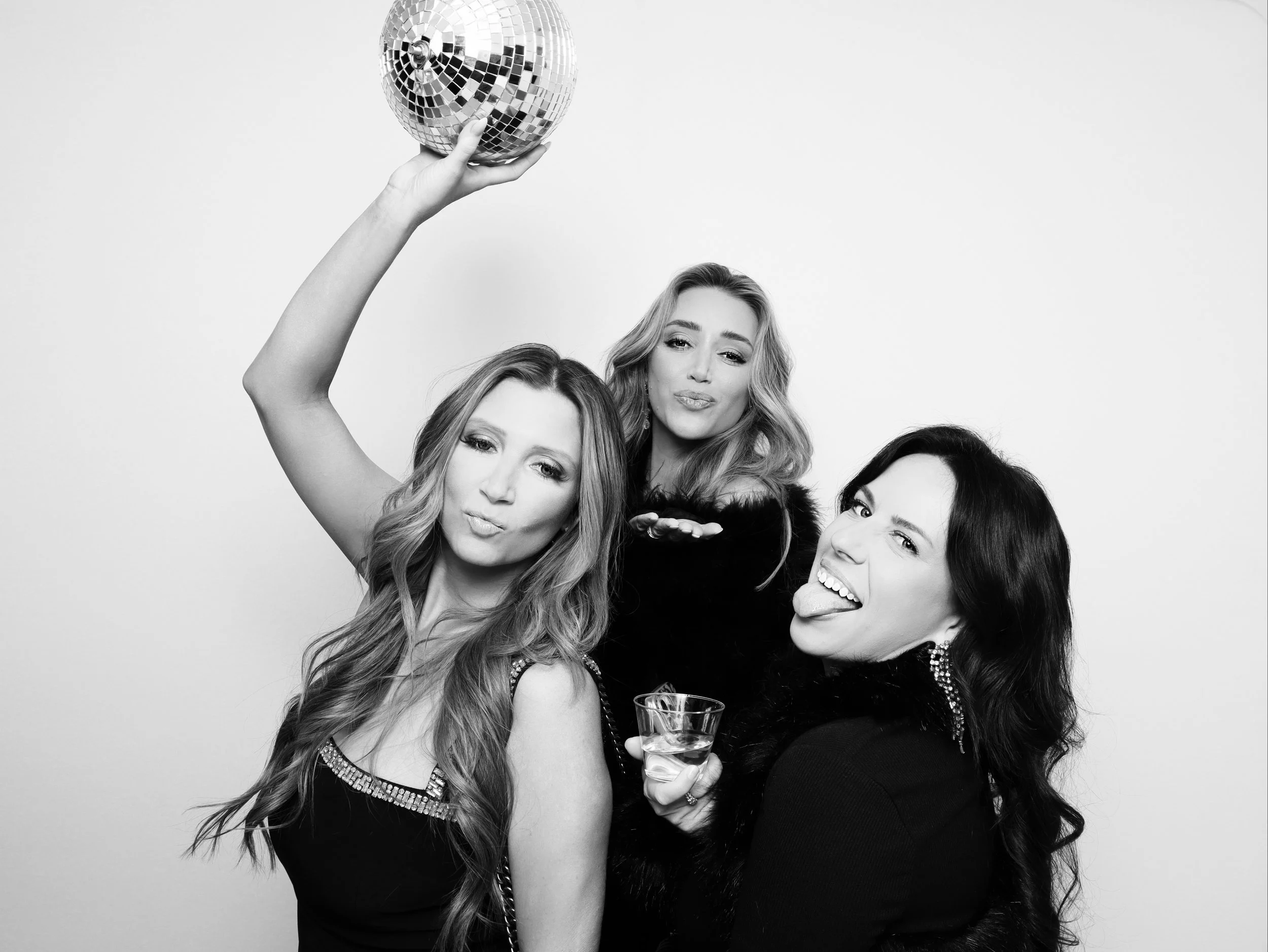 Three women celebrating with a disco ball, one holding it overhead, all making playful faces.