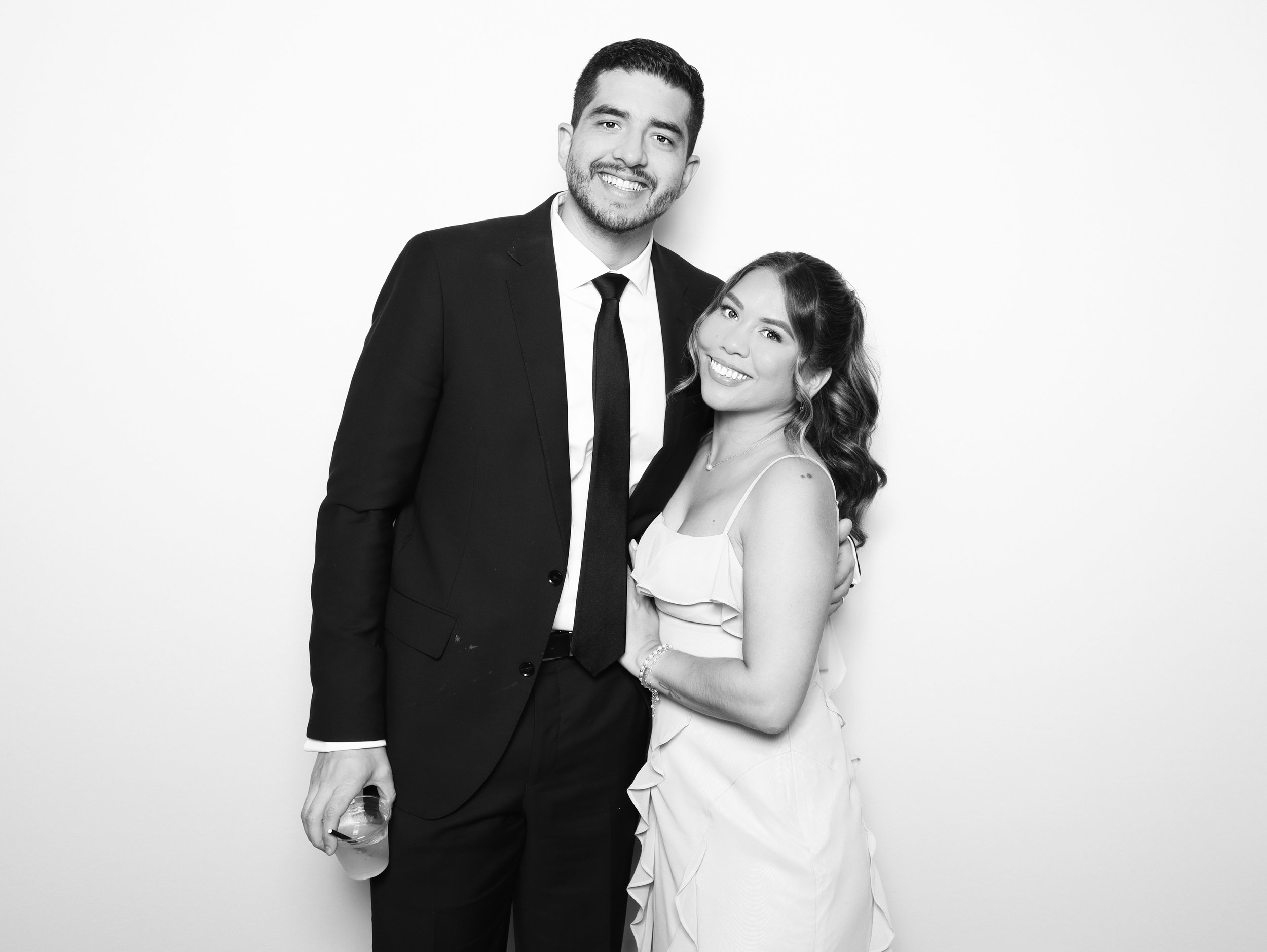 A black-and-white photo of a smiling man in a suit and a woman in a dress standing close together against a plain white background.