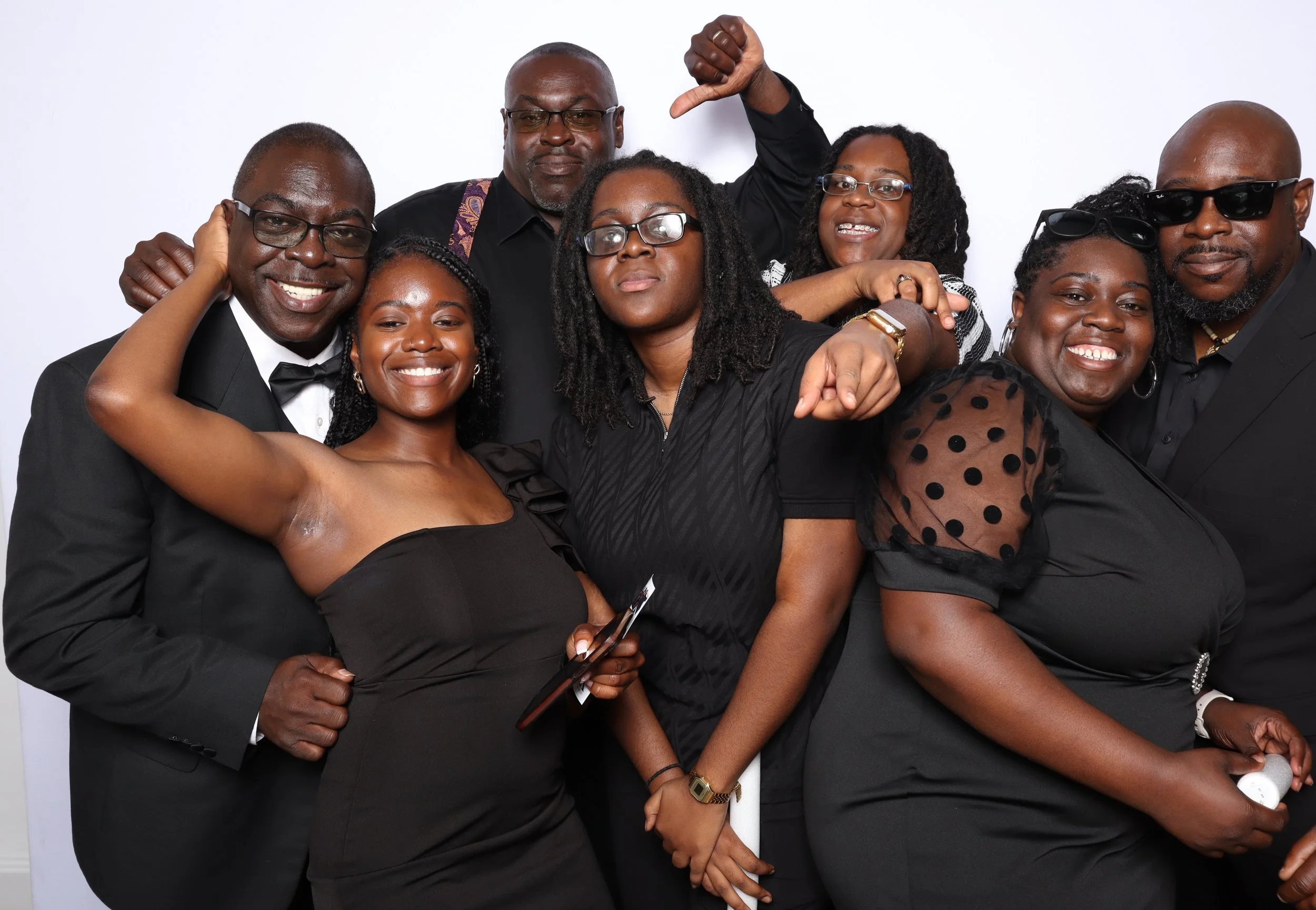 Group of eight diverse adults dressed in black formal attire, posing together at a celebration or event.