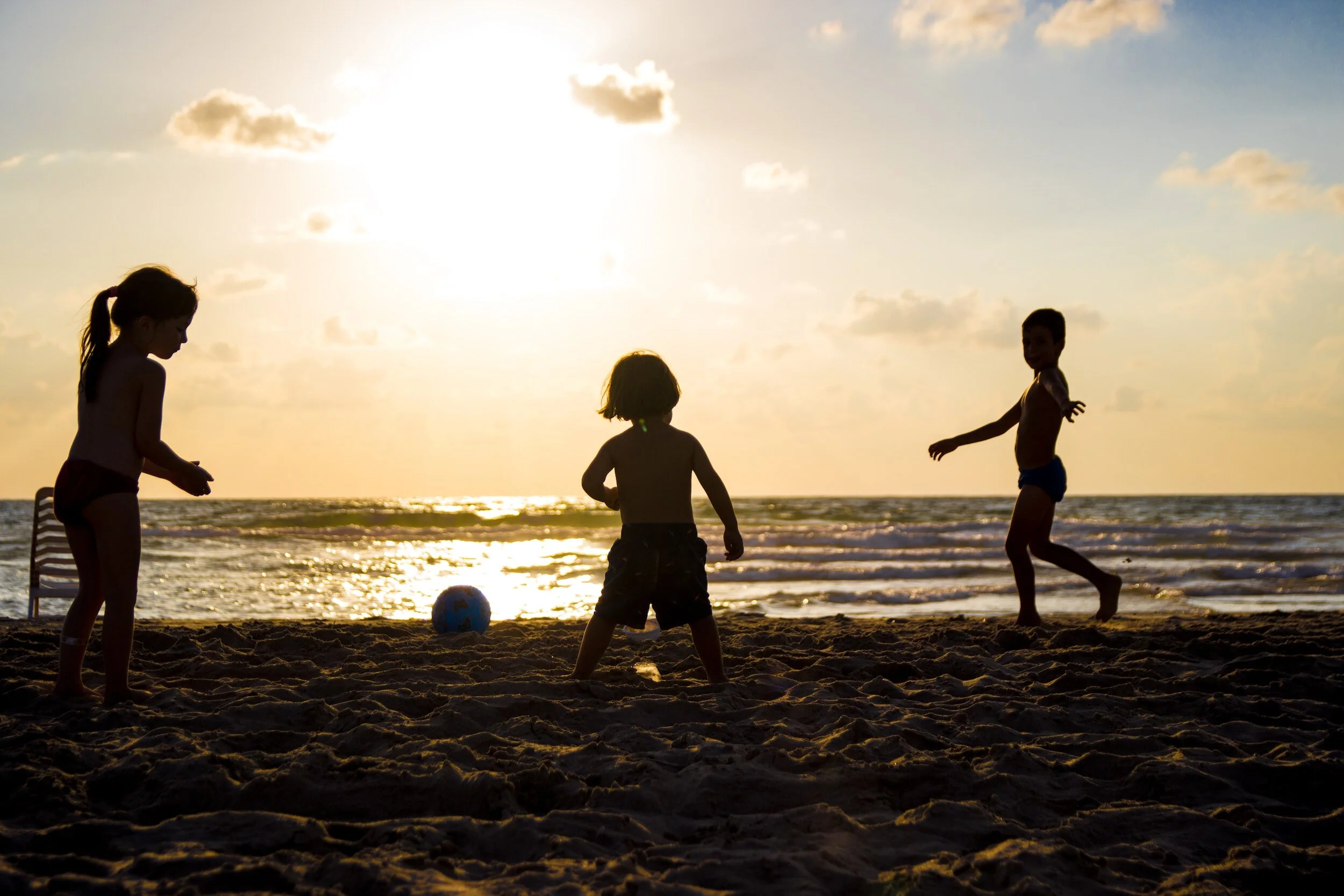 Children playing soccer on the beach at sunset.
